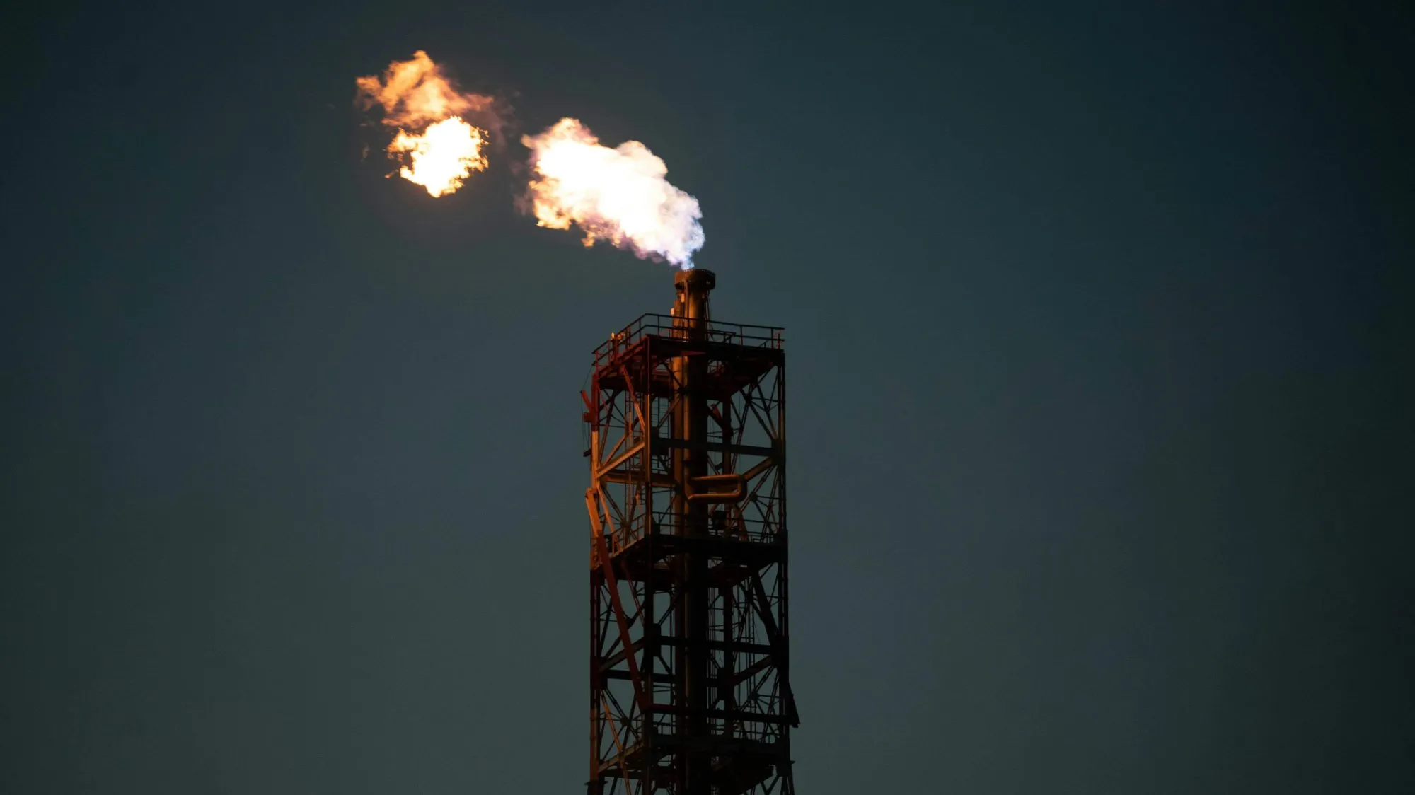 Industrial flare stack burning off gas against a dark night sky.