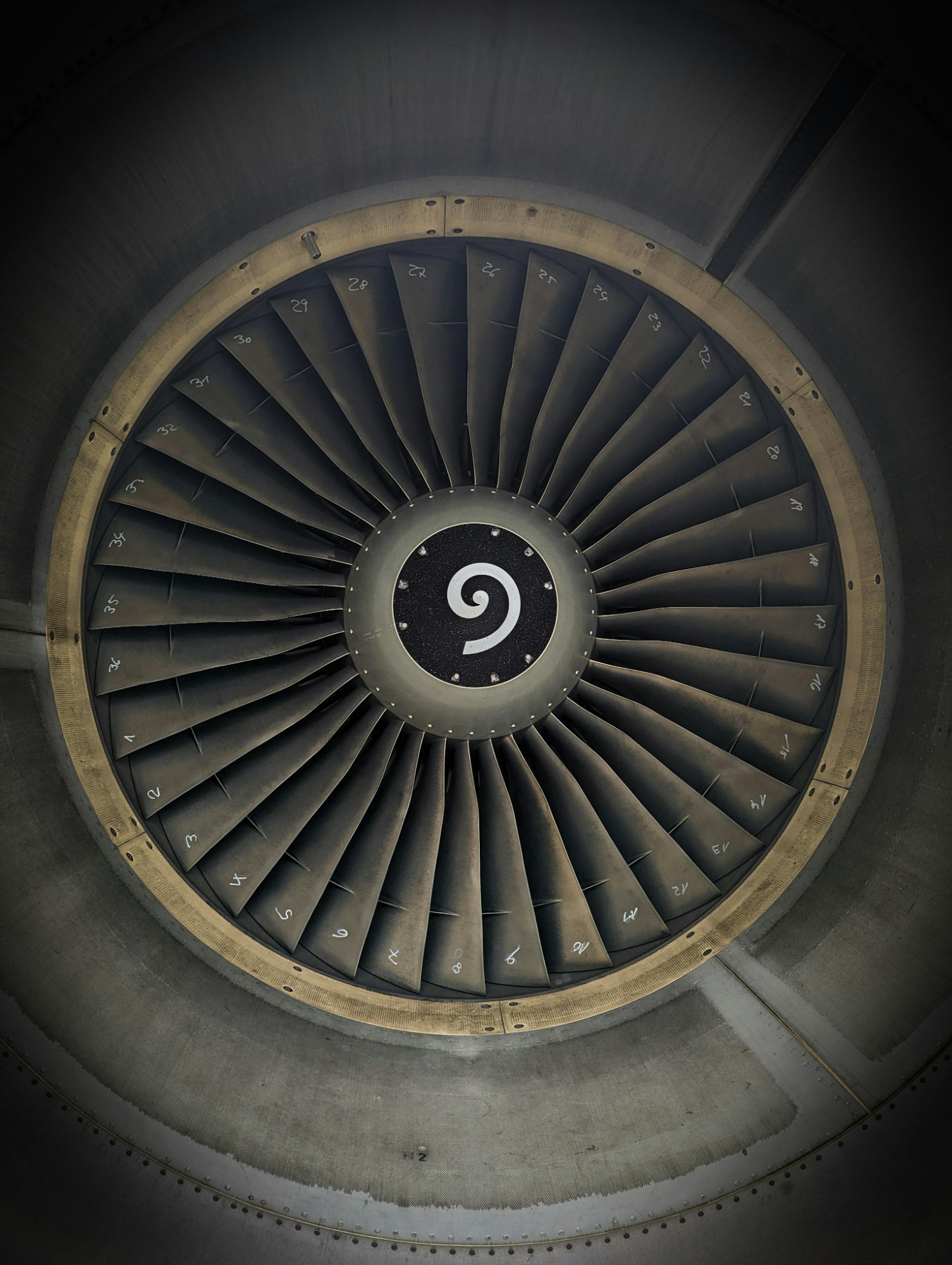 Close-up view of an aircraft jet engine turbine with numbered fan blades and a spiral design in the center.