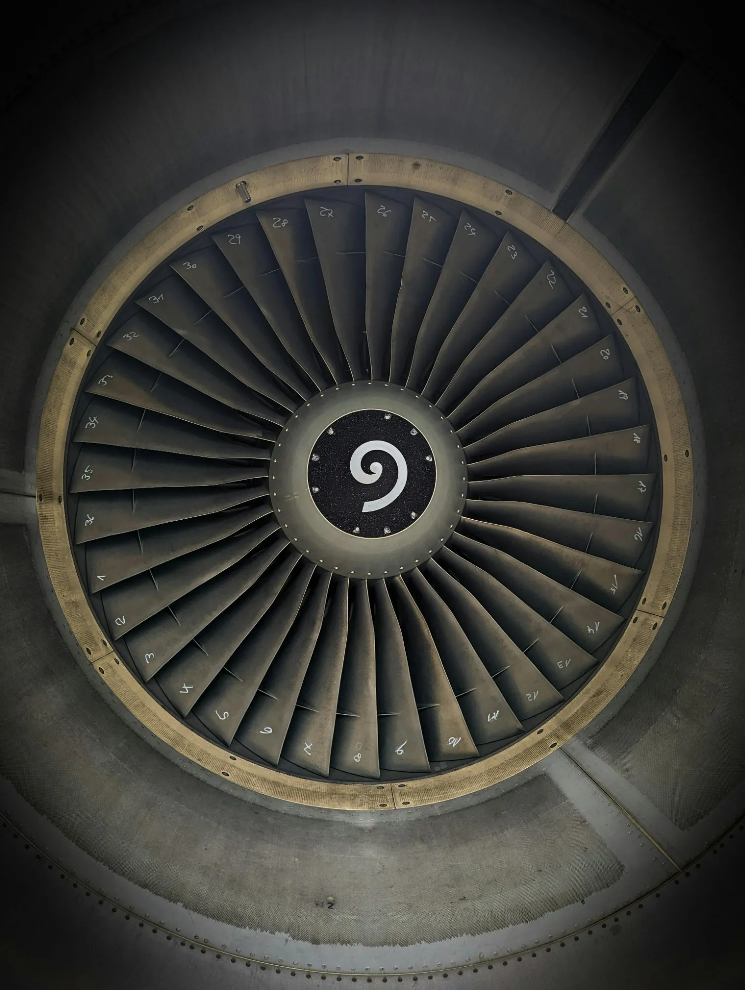 Close-up view of an aircraft jet engine turbine with numbered fan blades and a spiral design in the center.