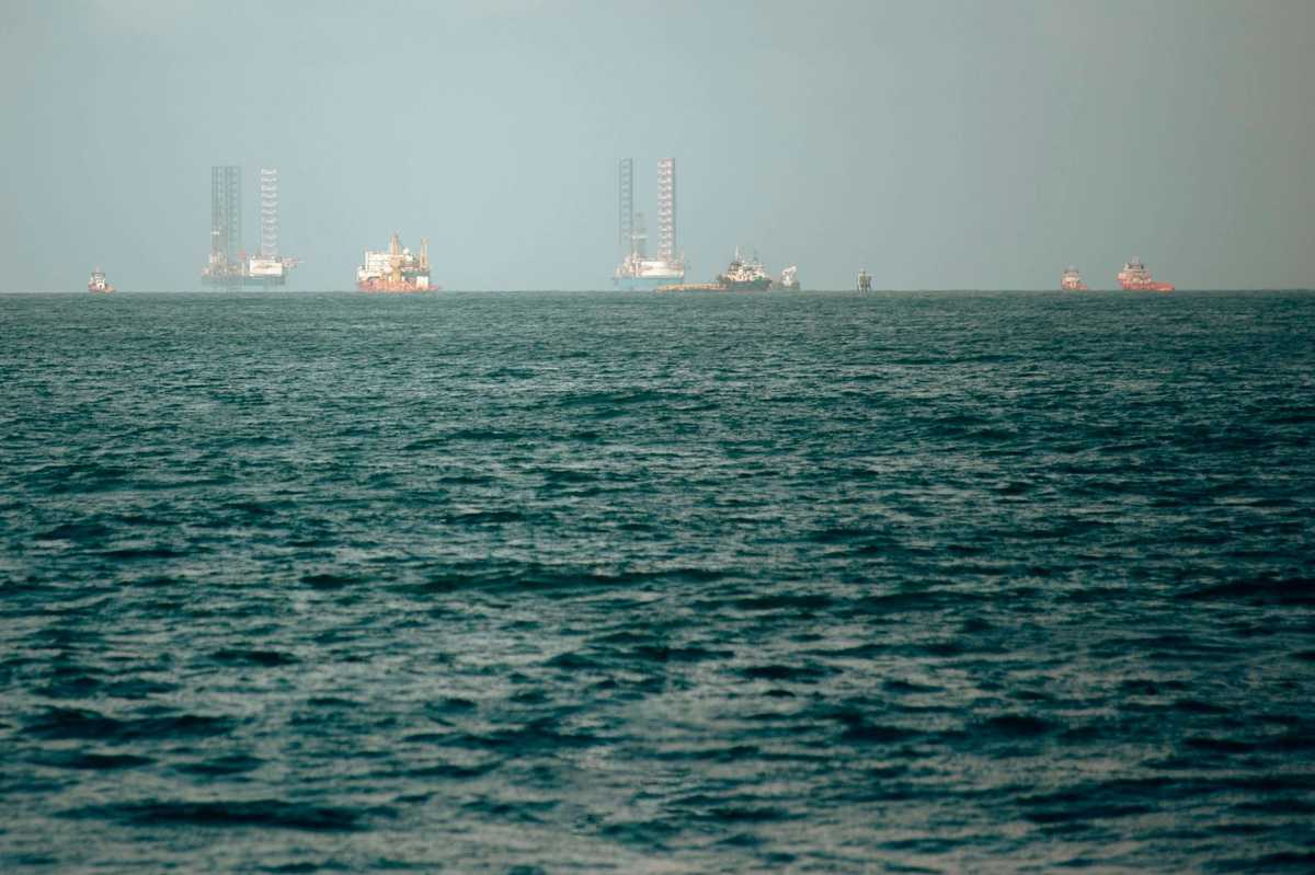 Offshore oil rigs and support ships positioned on a calm sea under a clear sky.