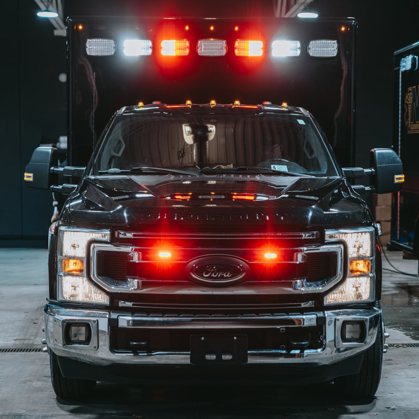 Front view of a black Ford emergency vehicle with red and white flashing lights on the grille and top.