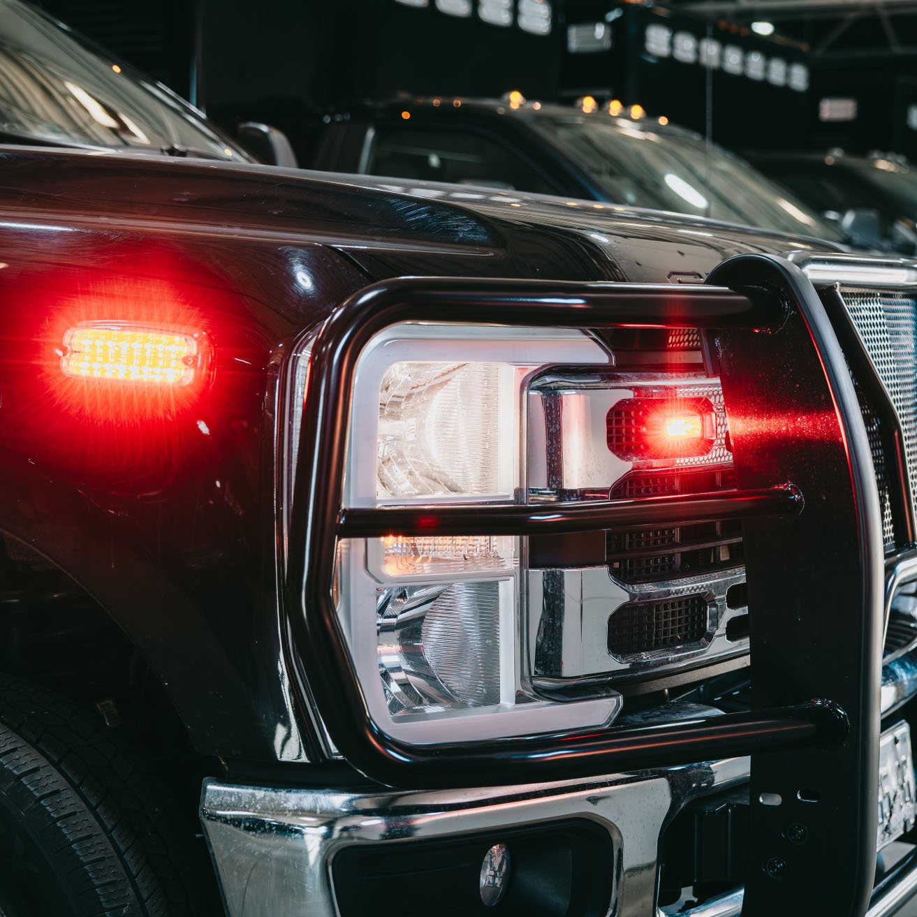 Close-up of a black truck's front corner with illuminated red signal lights and a grille guard.