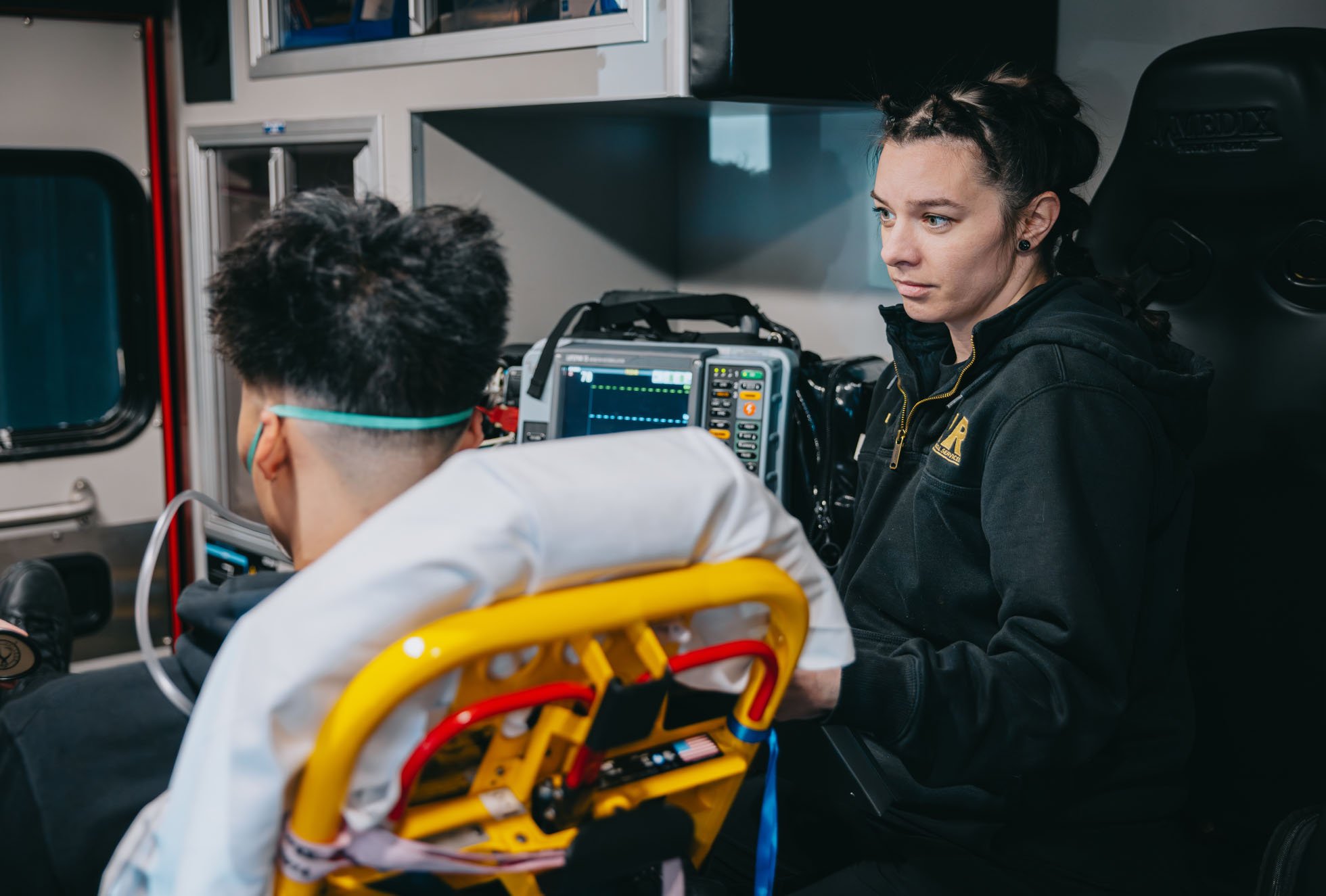 Paramedic attending to a patient in an ambulance with medical monitor and equipment visible.