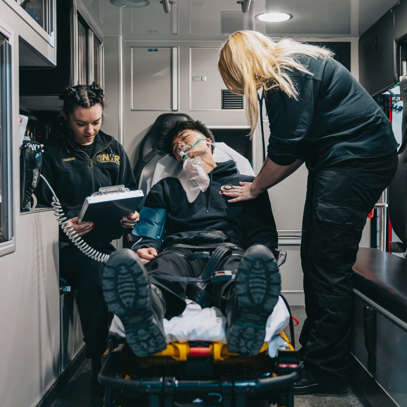 Two EMTs attending to an unconscious patient with oxygen mask inside an ambulance.