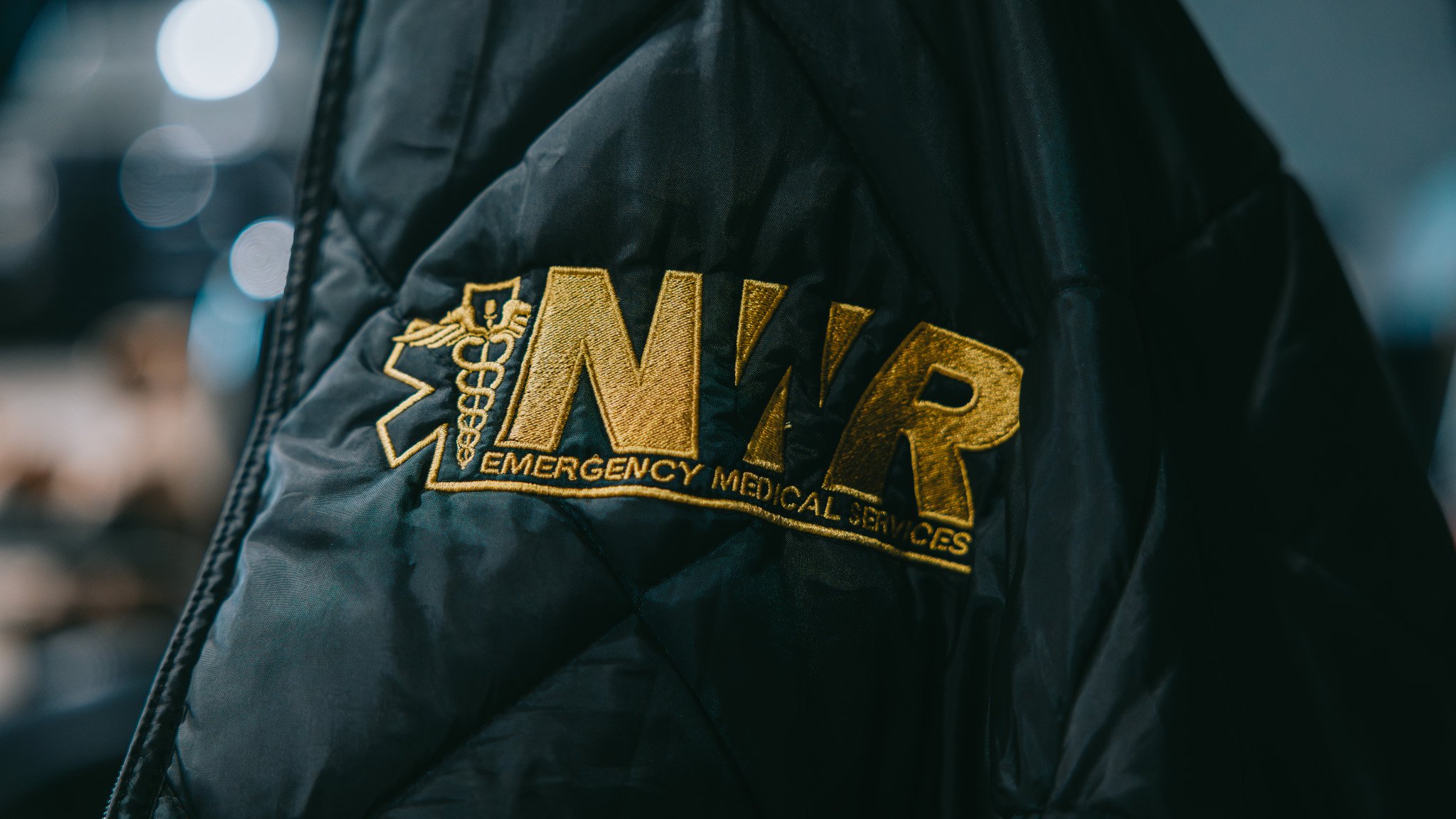 Black jacket with gold embroidered NWR and Emergency Medical Services insignia and caduceus symbol.