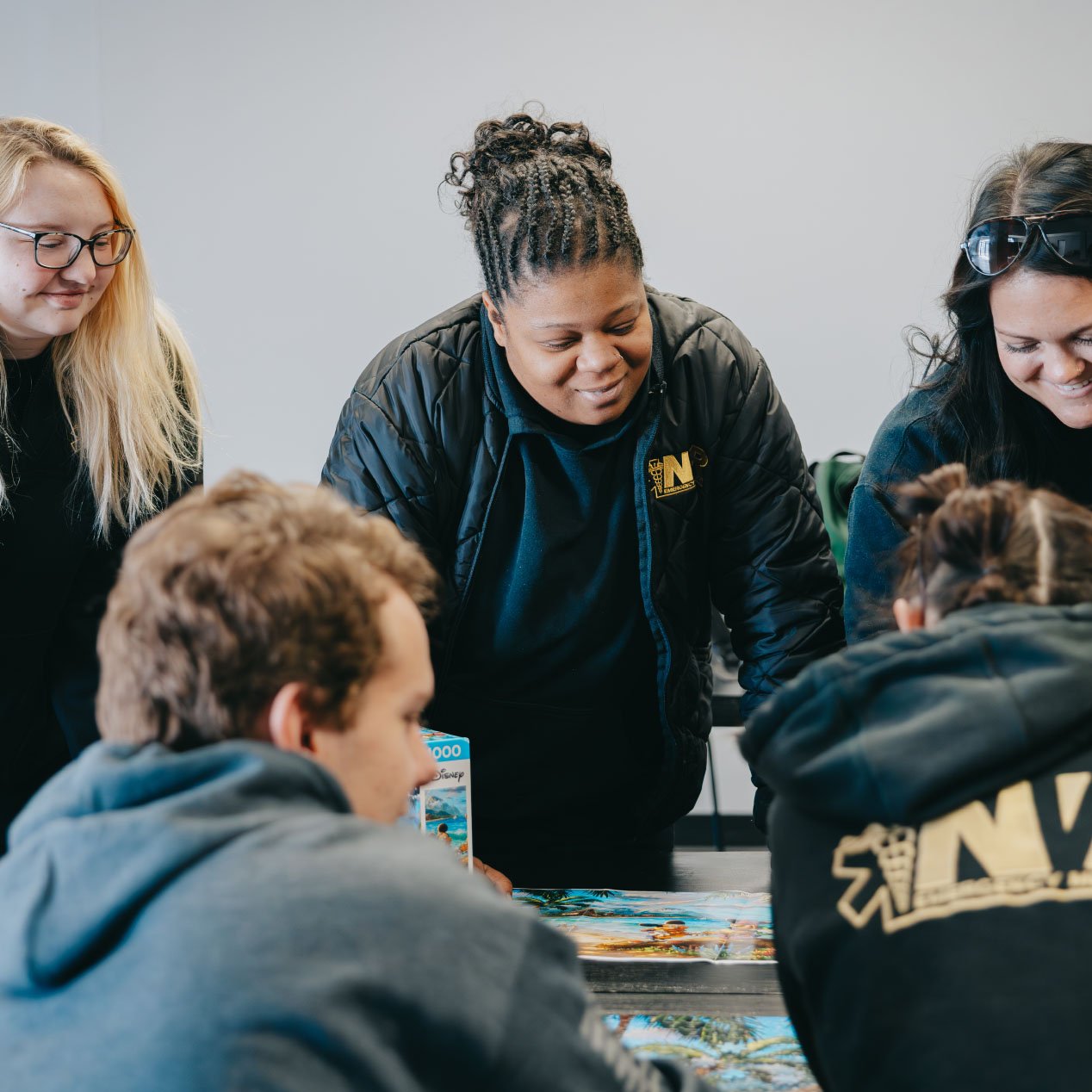 Five people gathered around a table, looking at a puzzle they are assembling together.