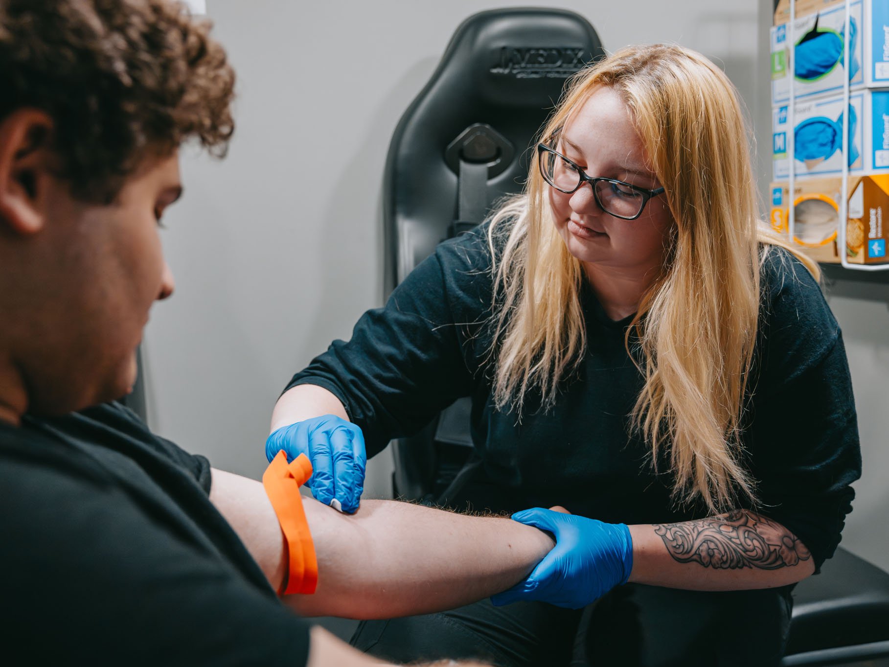 Healthcare professional wearing blue gloves applies a tourniquet to a patient's arm preparing for a blood draw.
