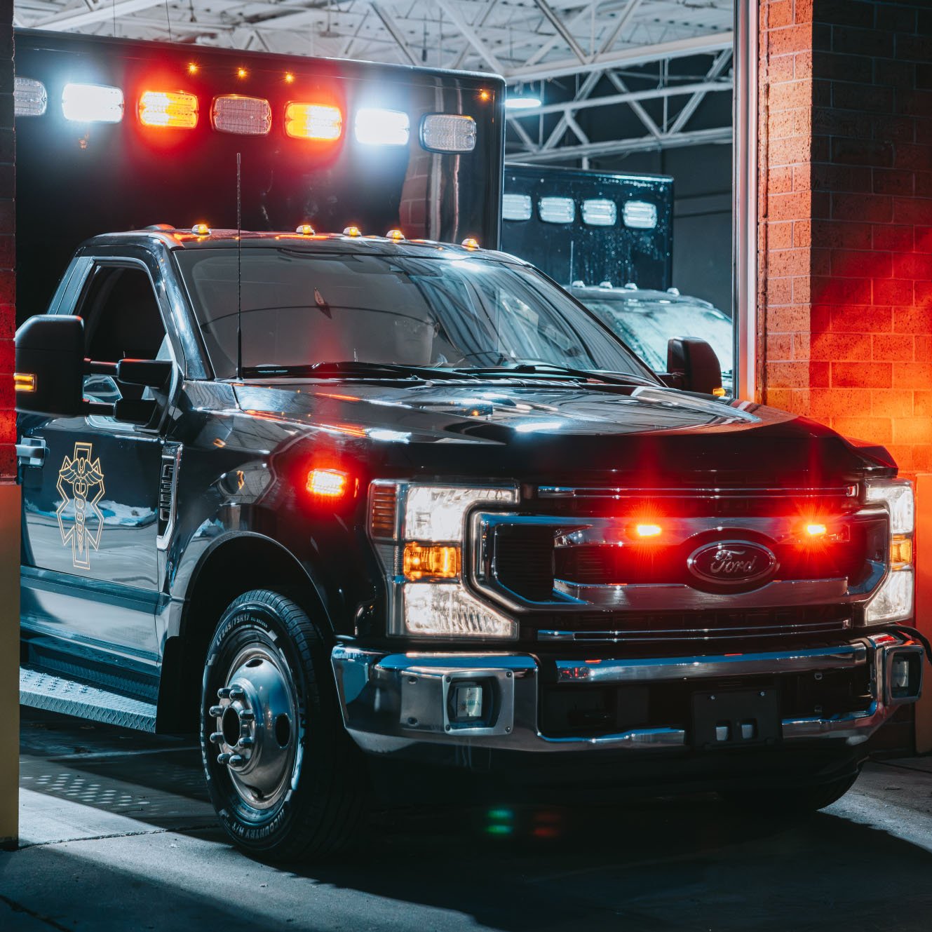 Black Ford emergency response vehicle with flashing red and white lights parked inside a garage with brick walls.