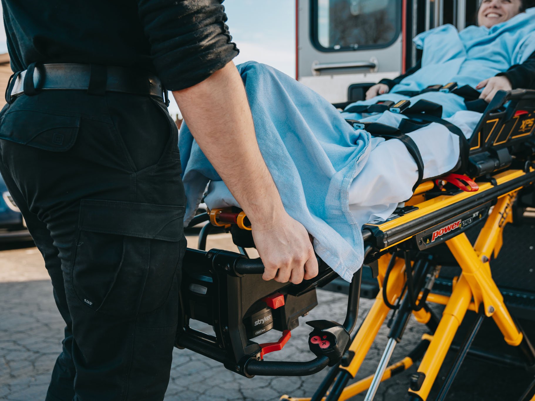 Paramedic pushing a stretcher with a patient covered in a blue blanket towards an ambulance.