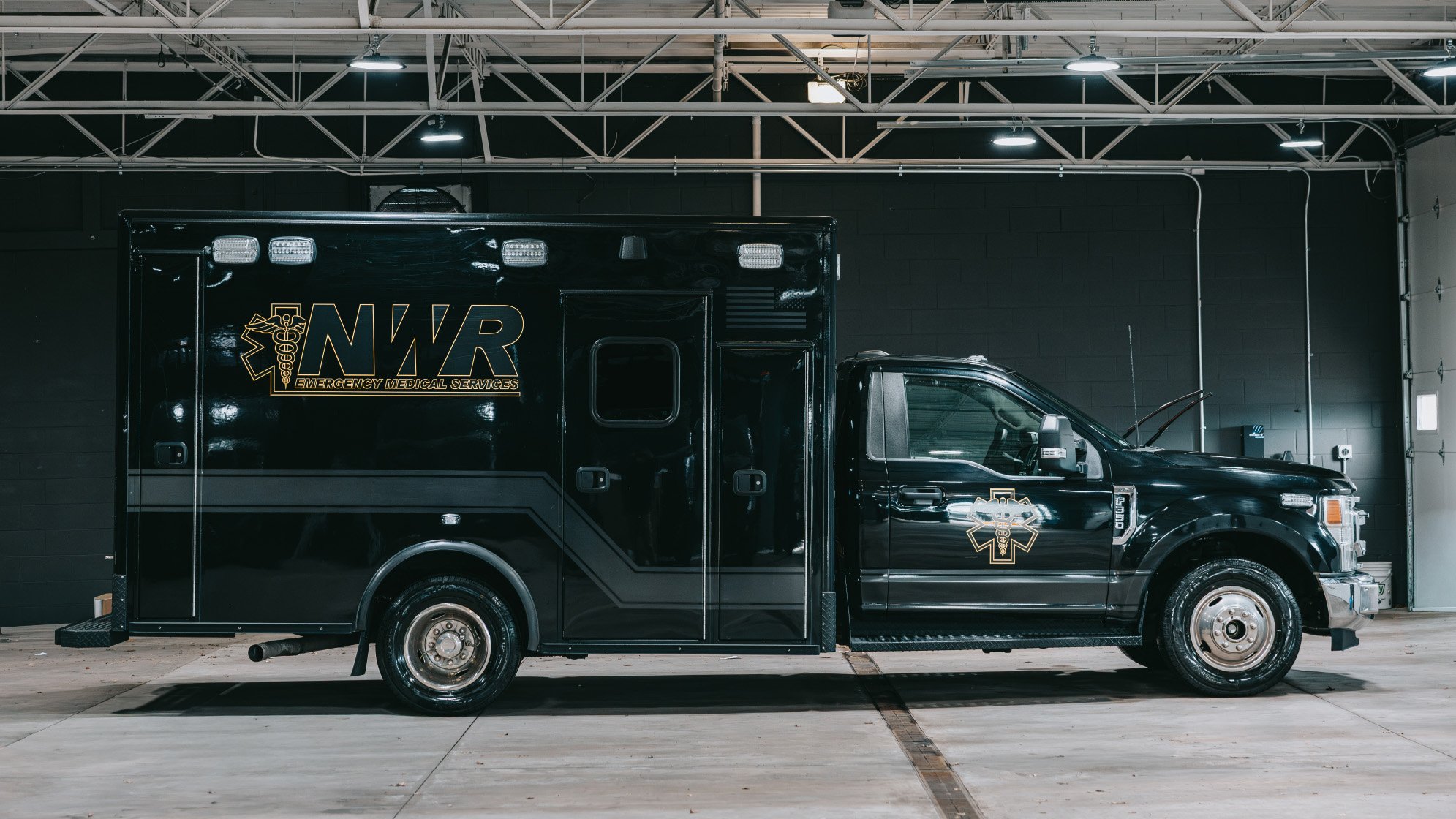 Black emergency medical services ambulance truck parked inside a garage with 'NWR Emergency Medical Services' logo on the side.