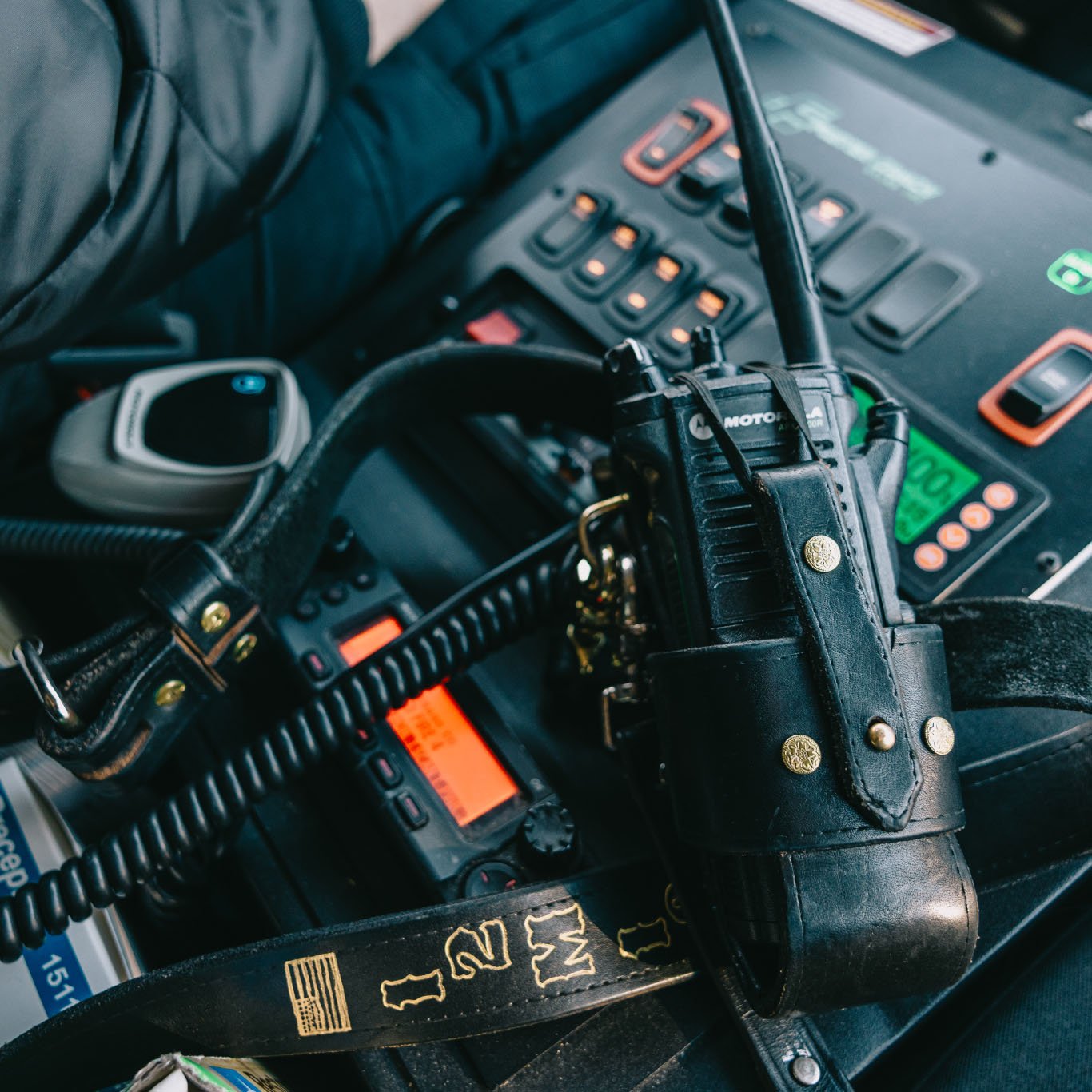 Close-up of a Motorola walkie-talkie in a black leather holster resting on a vehicle control panel with illuminated buttons and screens.