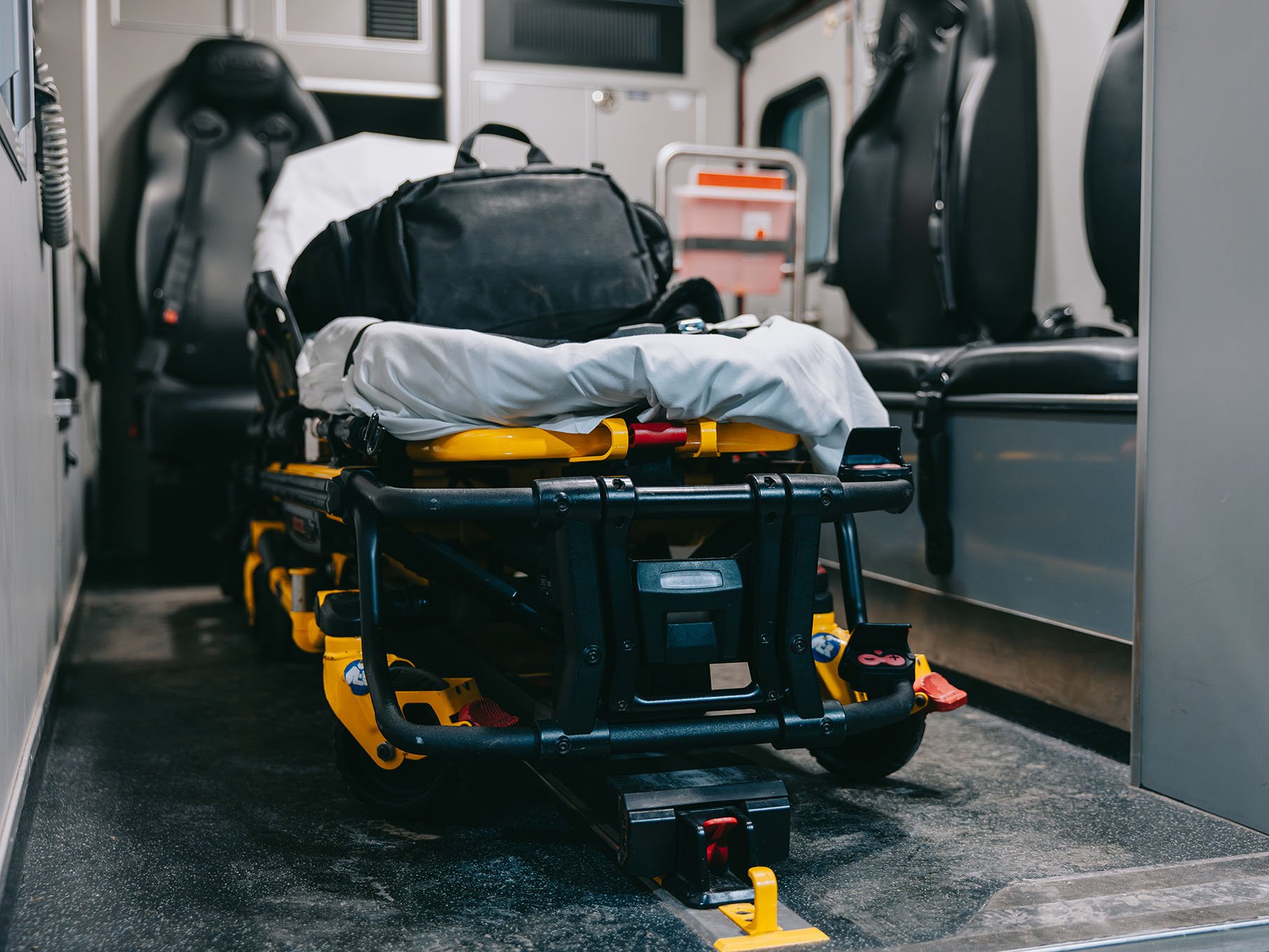 Empty ambulance stretcher with black bag and white sheet inside an ambulance interior.