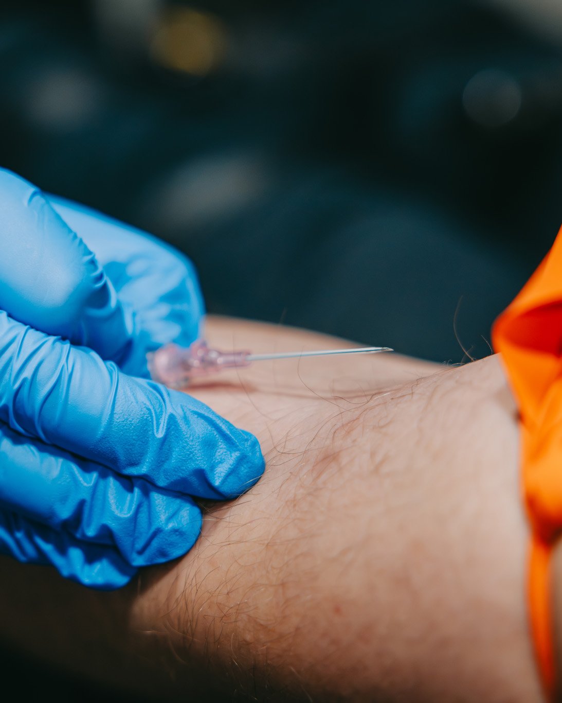 Close-up of gloved hand holding a syringe needle poised above a forearm for injection.