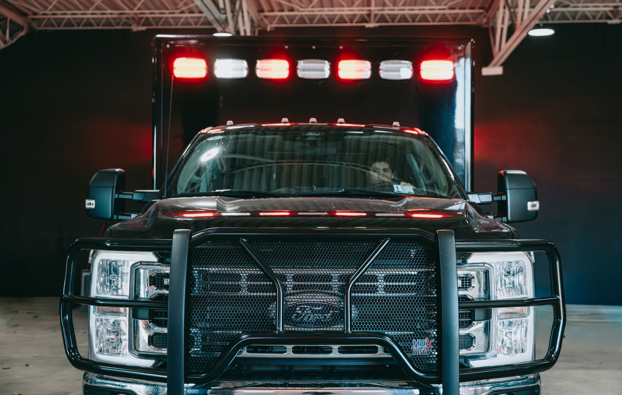 Front view of a black Ford truck with red and white emergency lights on top and a grille guard.