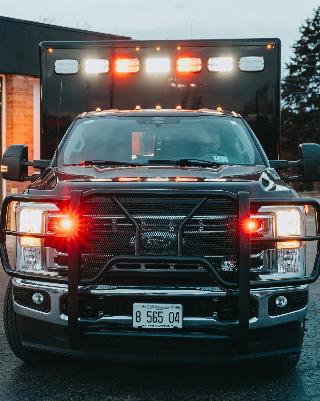 Front view of a black Ford ambulance with red and white emergency lights flashing and an Illinois license plate.