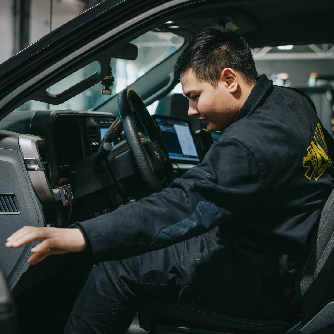 Man in black emergency services uniform sitting inside a vehicle, reaching toward the dashboard.