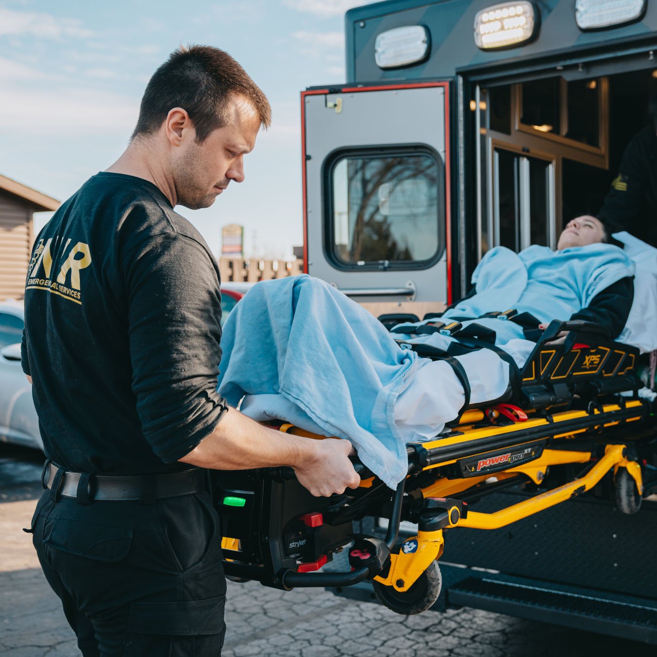 Paramedic loading a patient covered with a blue blanket on a stretcher into an ambulance.
