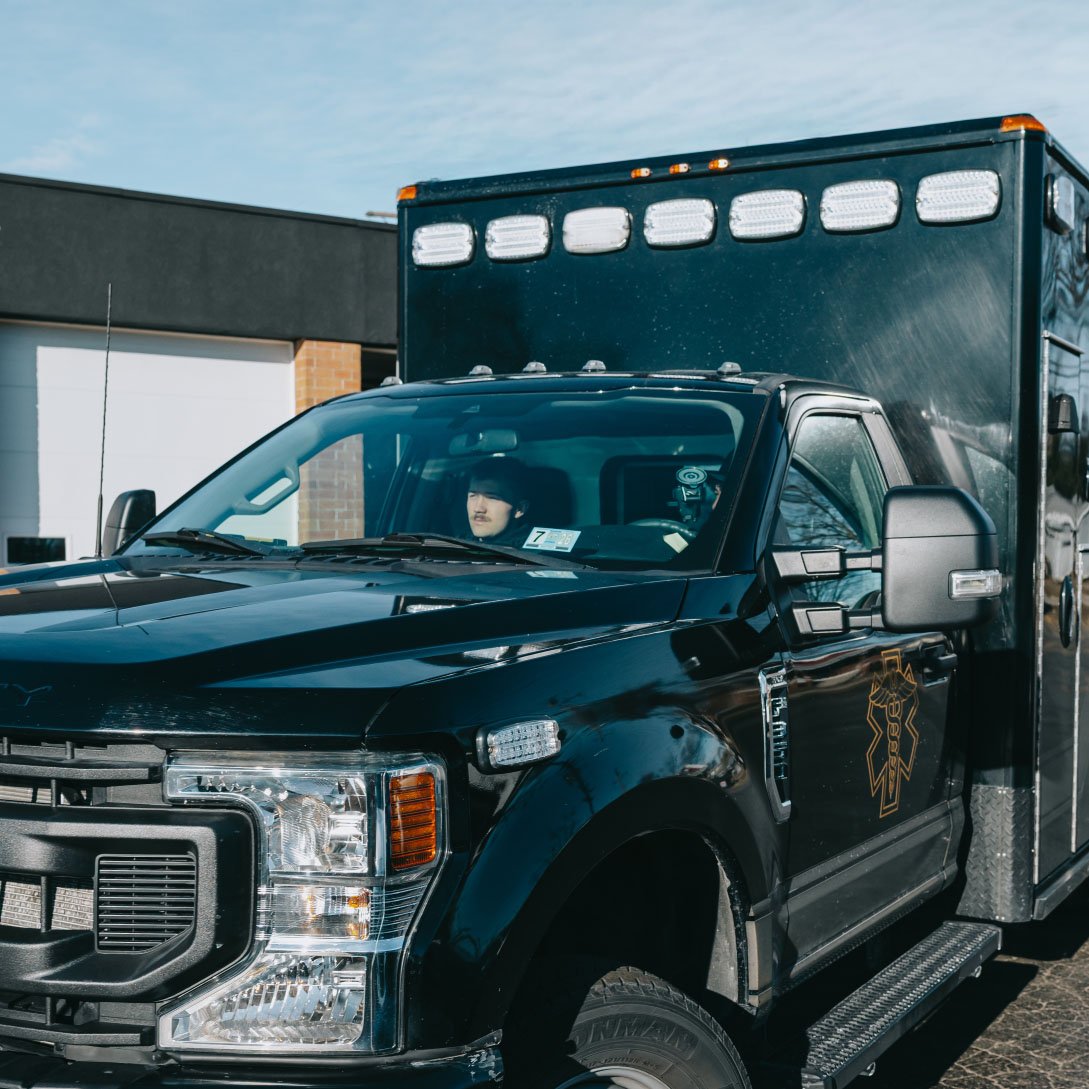 Black emergency response vehicle with a driver visible through the windshield parked outside a building.