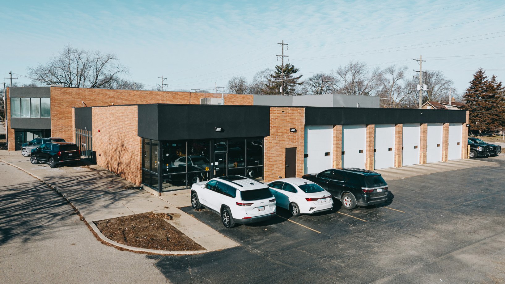 Commercial building with multiple garage doors, large windows, and a parking lot with several cars.