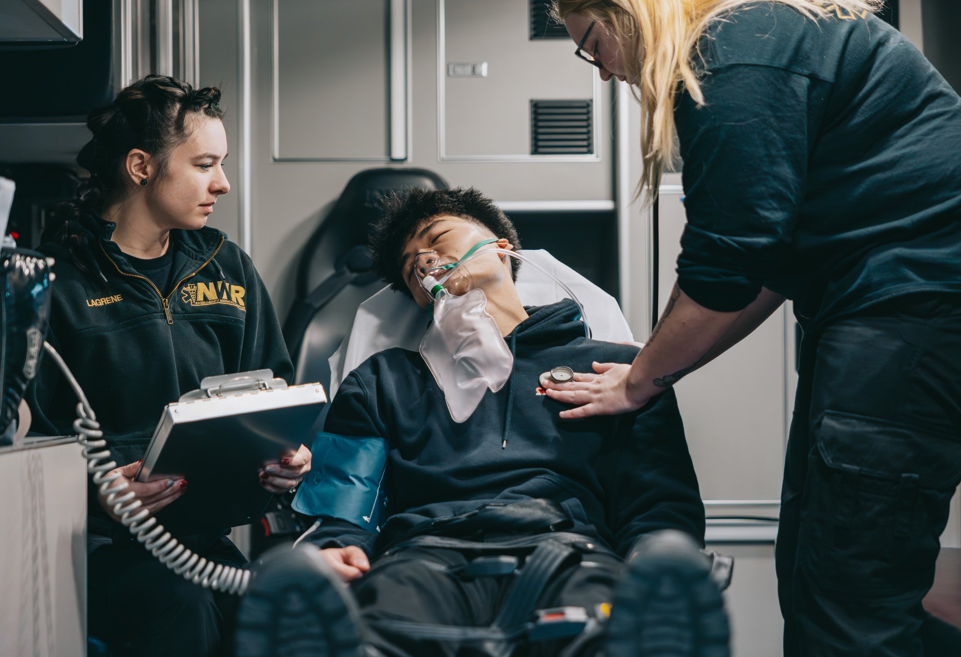 Two emergency medical responders attending to a patient with an oxygen mask inside an ambulance.