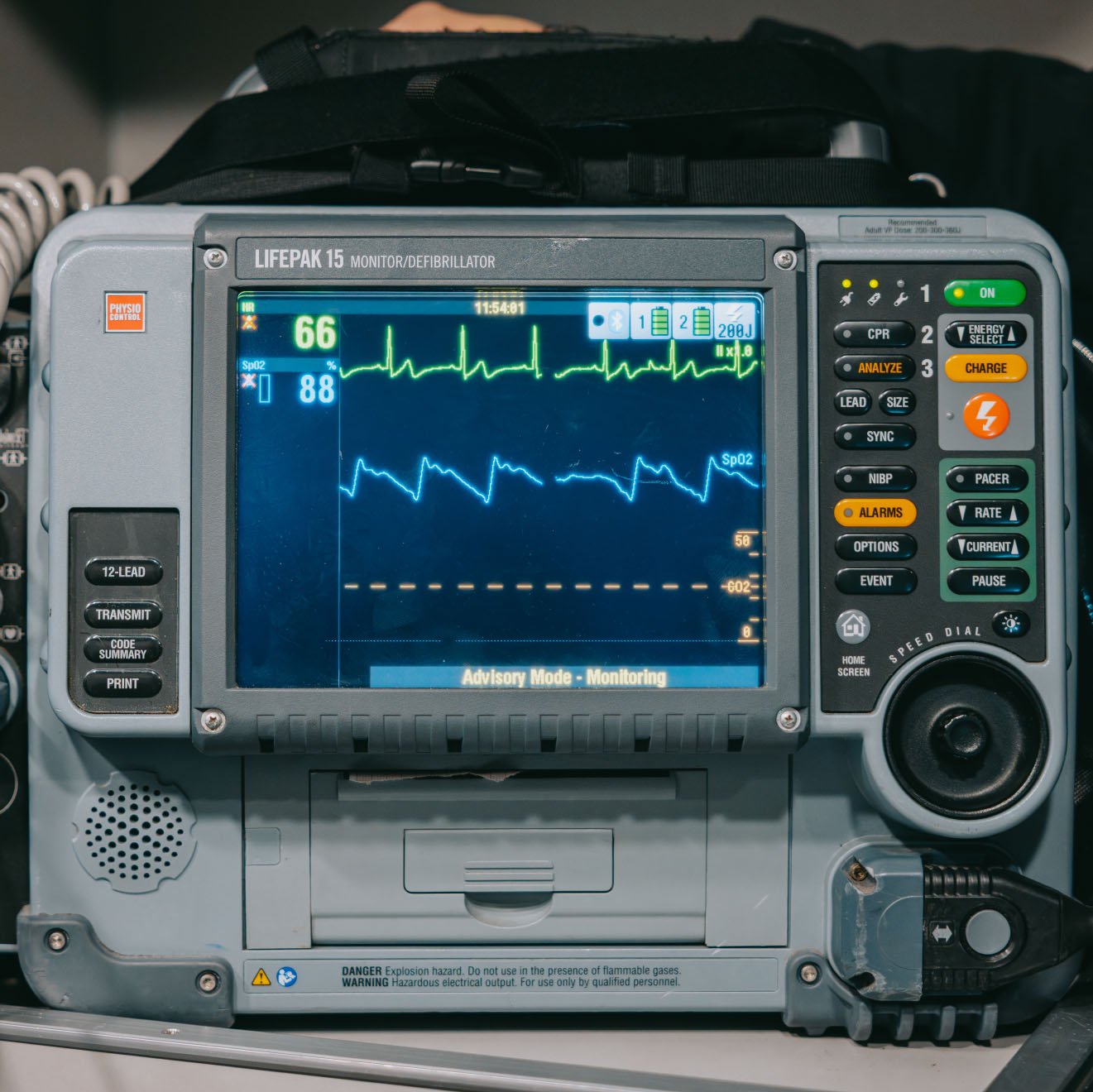 Close-up of a LIFEPAK 15 monitor/defibrillator showing heartbeat and oxygen saturation on screen with control buttons on the sides.