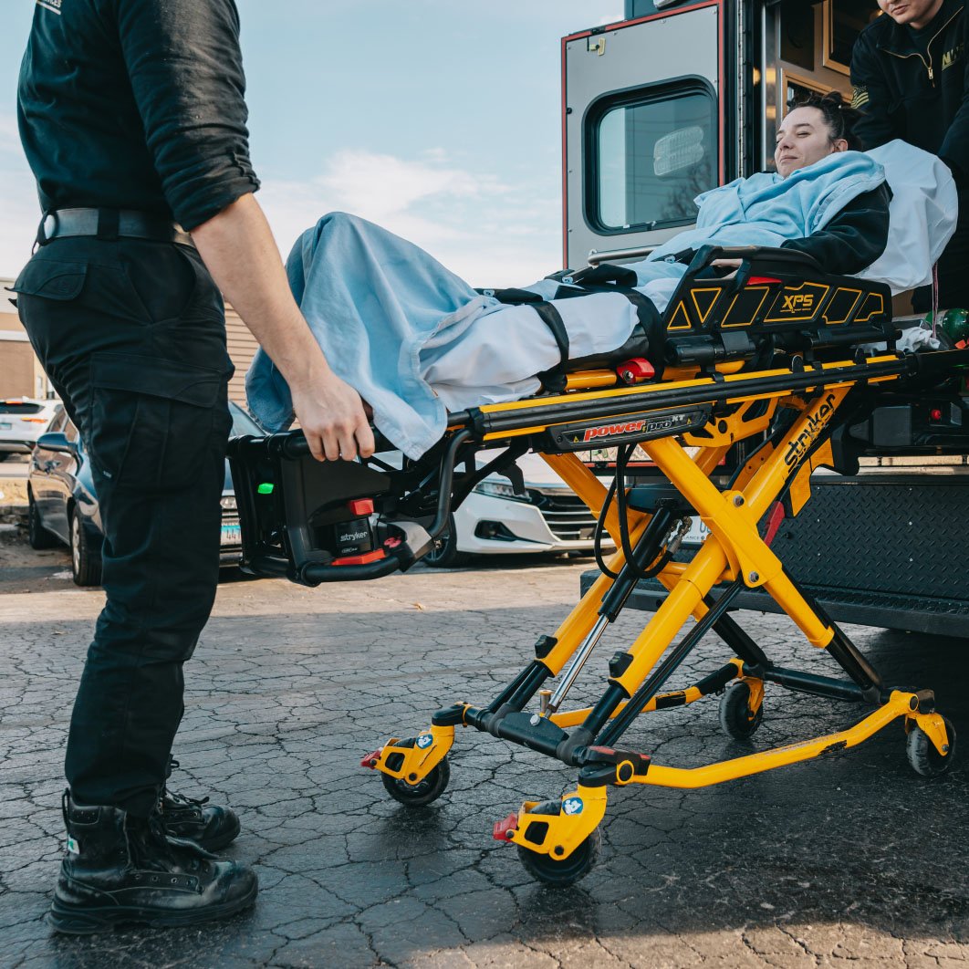Paramedics transporting a woman on a yellow stretcher into an ambulance.