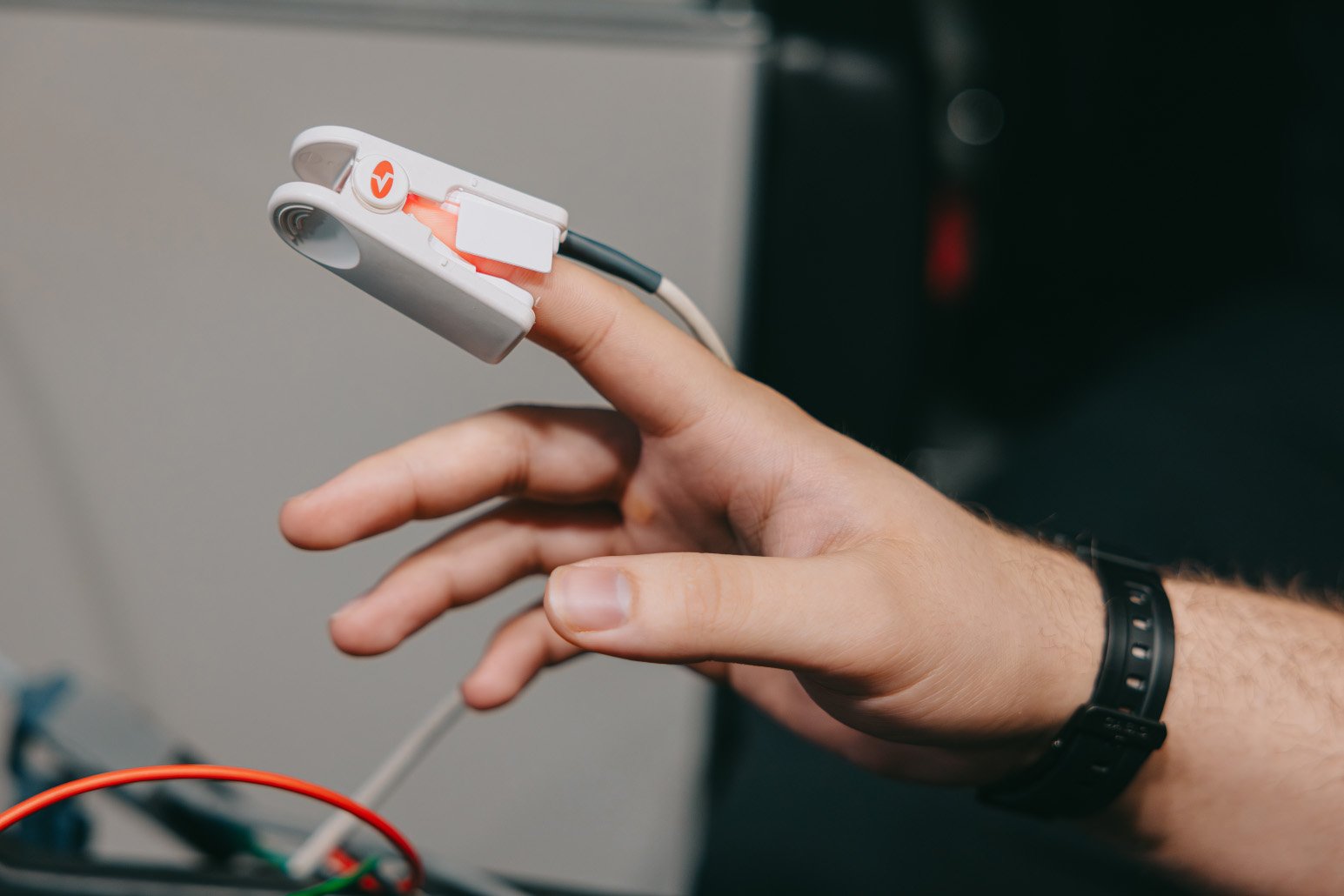 Hand wearing a pulse oximeter clipped to the index finger, measuring oxygen levels.