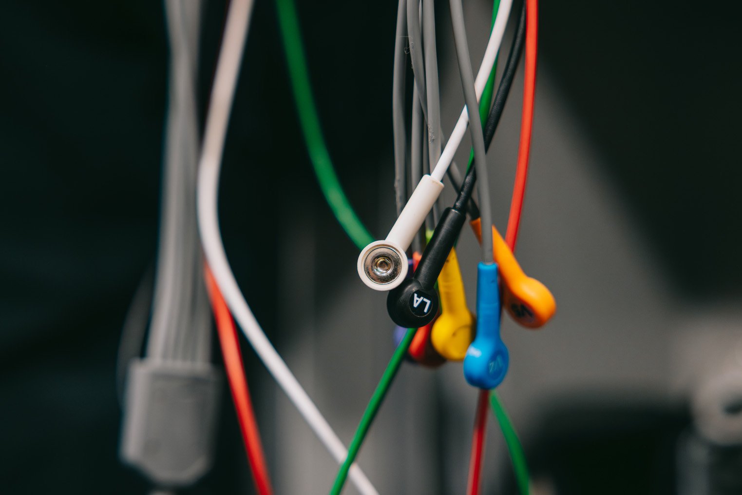 Close-up of colorful medical electrode wires with clips, labeled with letters and numbers.