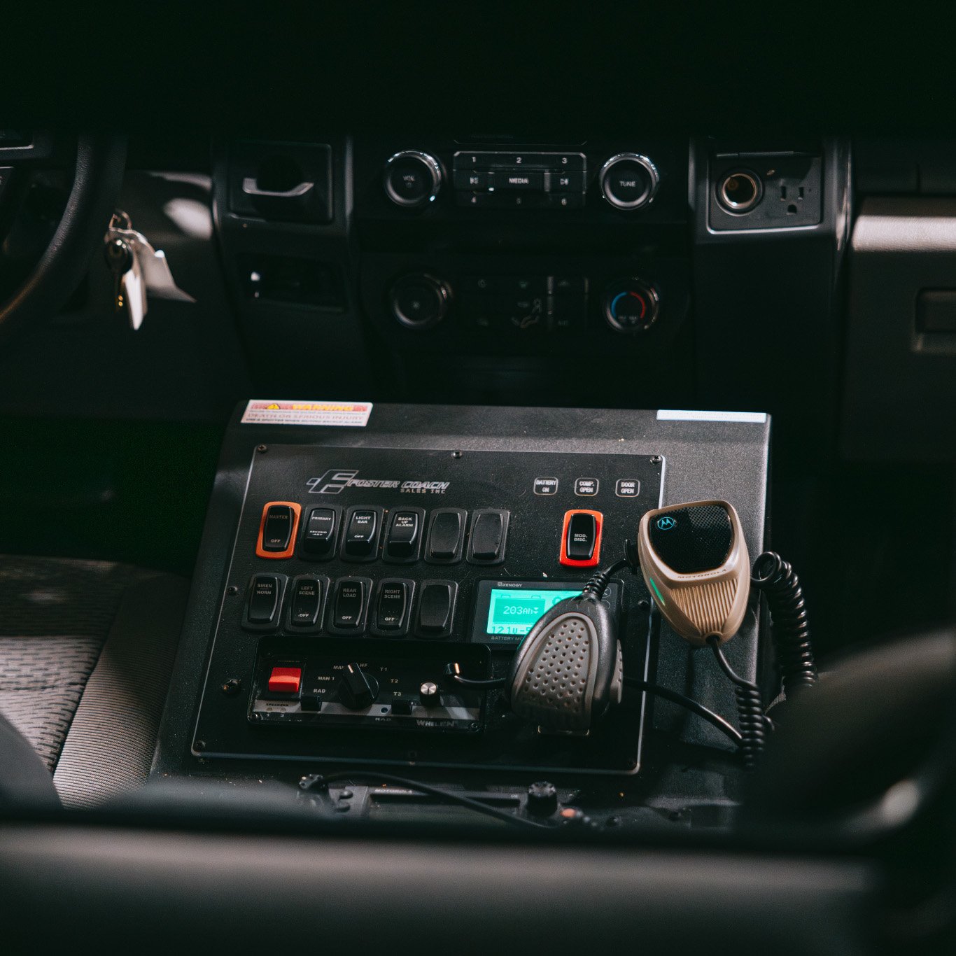 Control panel with switches, a radio microphone, and a digital display inside a vehicle cab.