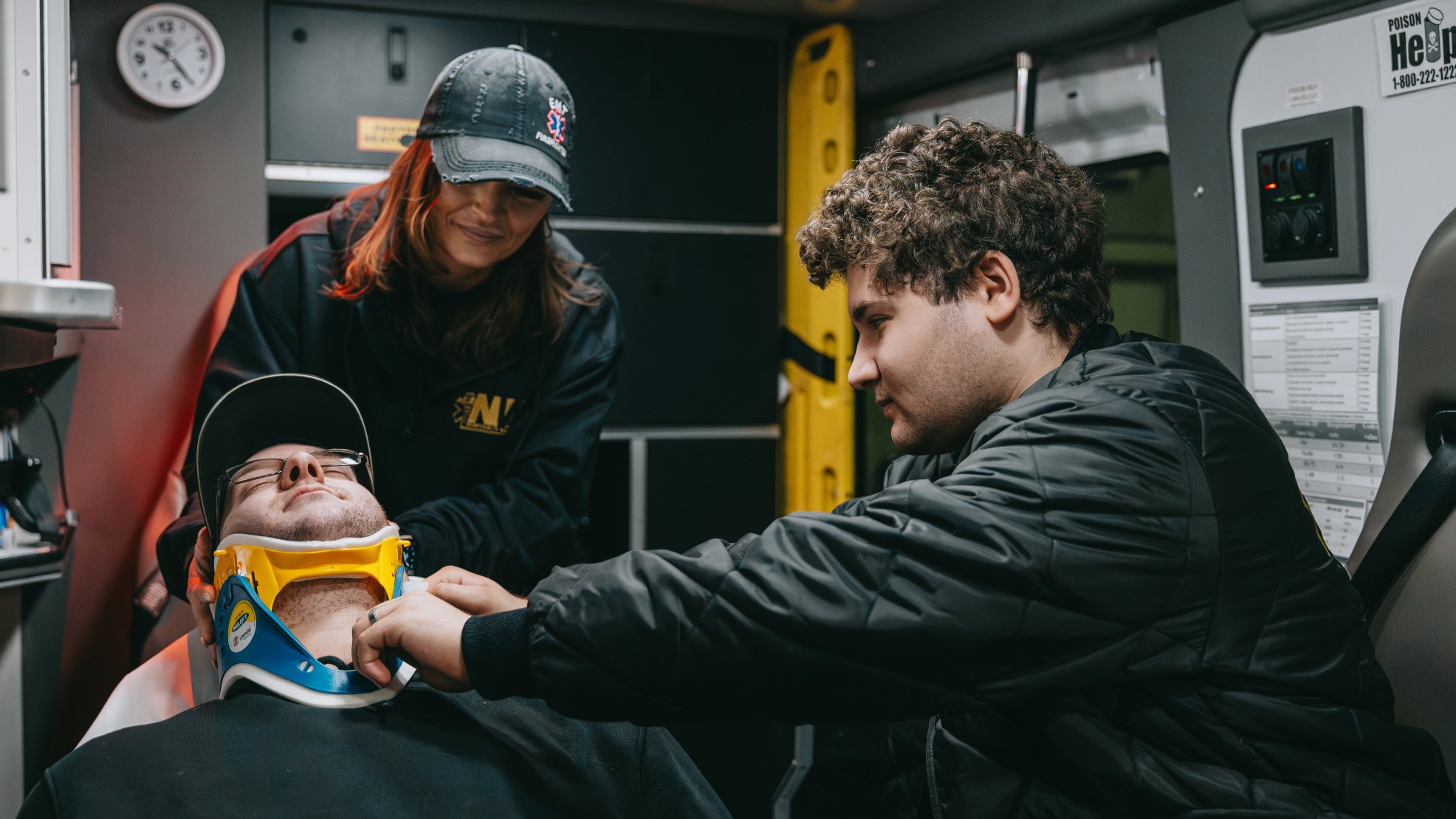 Two emergency medical technicians fitting a young man with a neck brace inside an ambulance.