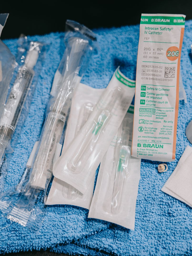 Medical supplies including individually packaged intravenous catheters and syringes arranged on a blue towel.