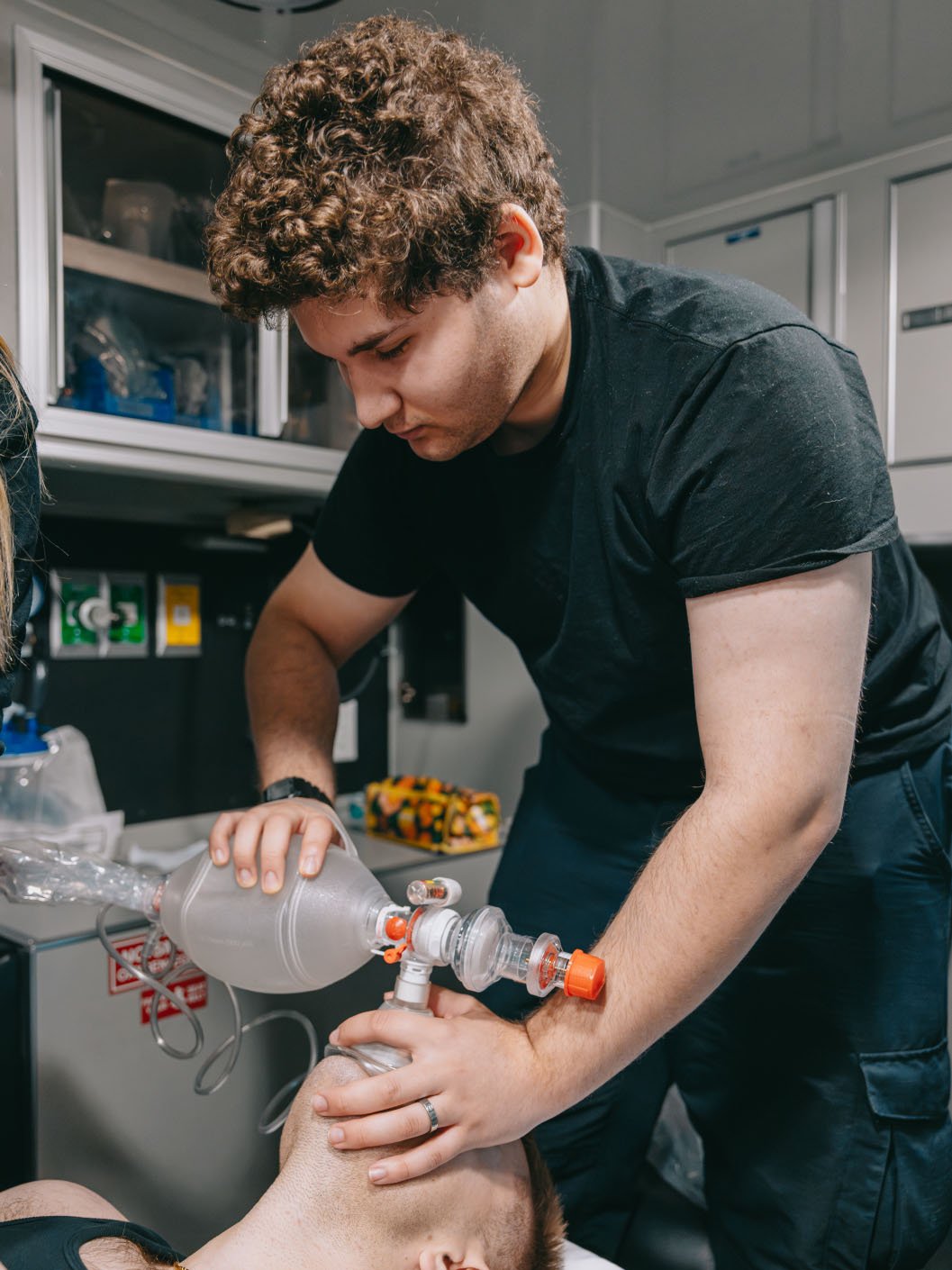 Emergency responder using a manual resuscitator to assist a person lying down.