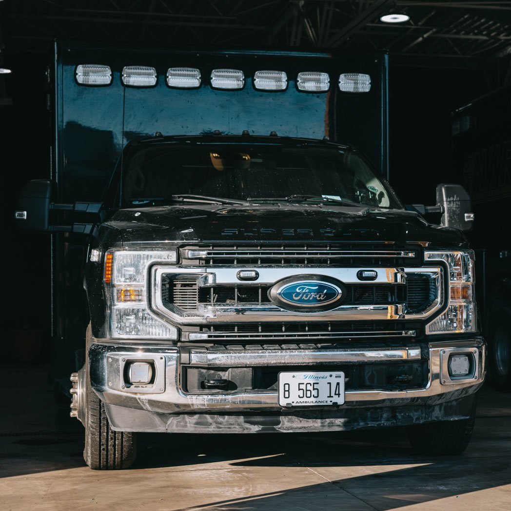 Front view of a black Ford ambulance truck with Illinois license plate parked indoors.