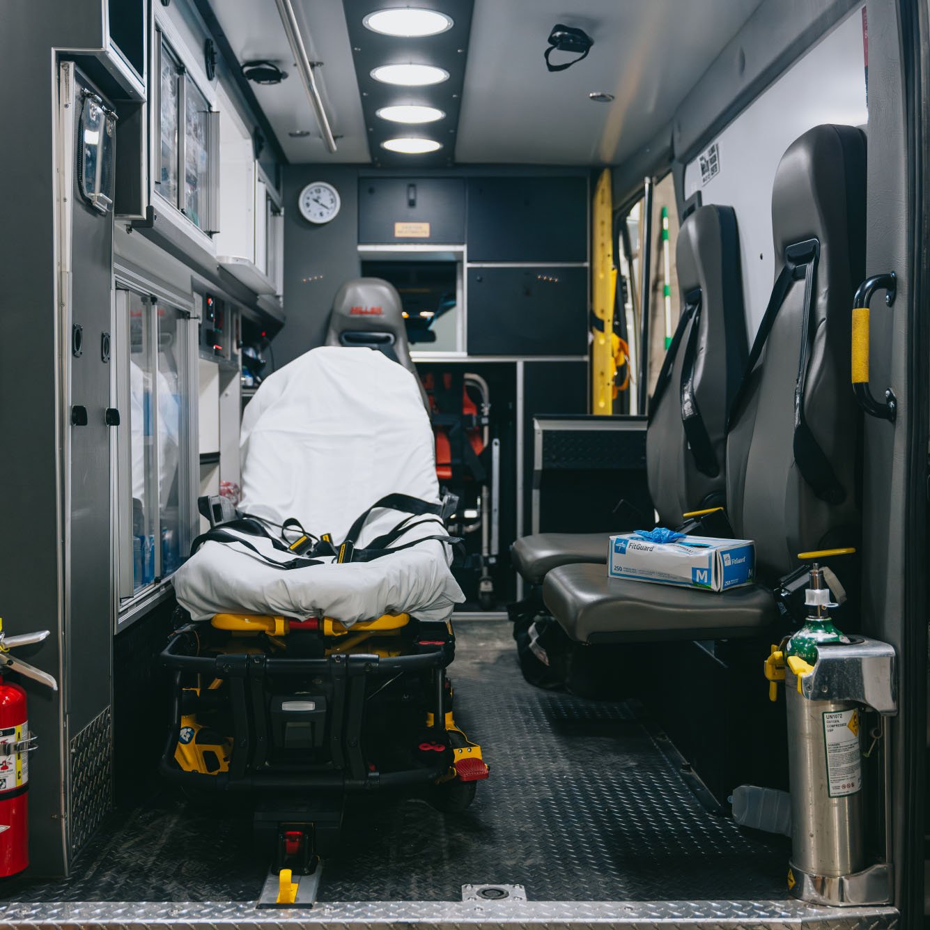 Interior of an ambulance showing a stretcher, two seats with seat belts, medical gloves box, and an oxygen tank.