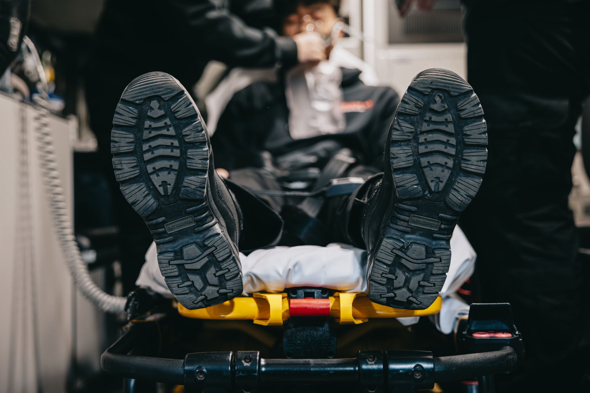 Person lying on a stretcher wearing black boots with sole tread visible, hands holding a mask near their face.