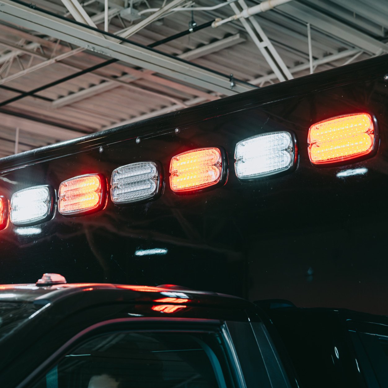 Close-up of alternating red and white emergency lights mounted on a black vehicle roof inside a garage.