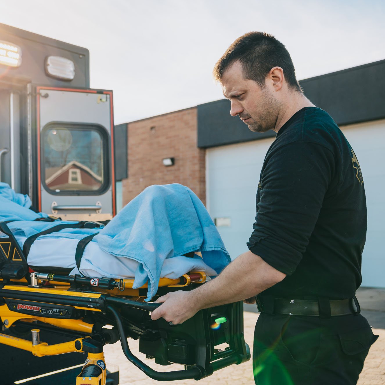 Paramedic preparing a stretcher with a patient covered by a blue blanket near an ambulance.