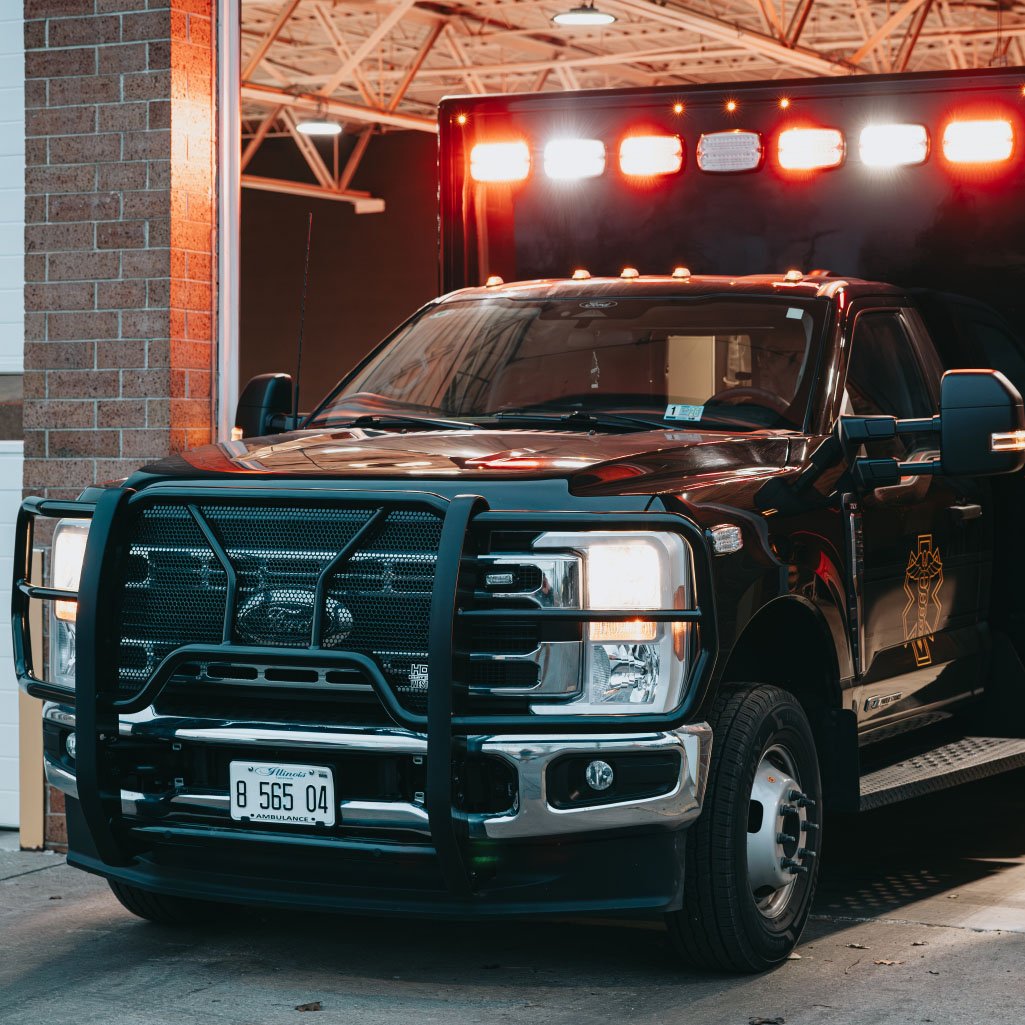 Front view of a black ambulance with flashing lights parked under a canopy next to a brick wall.