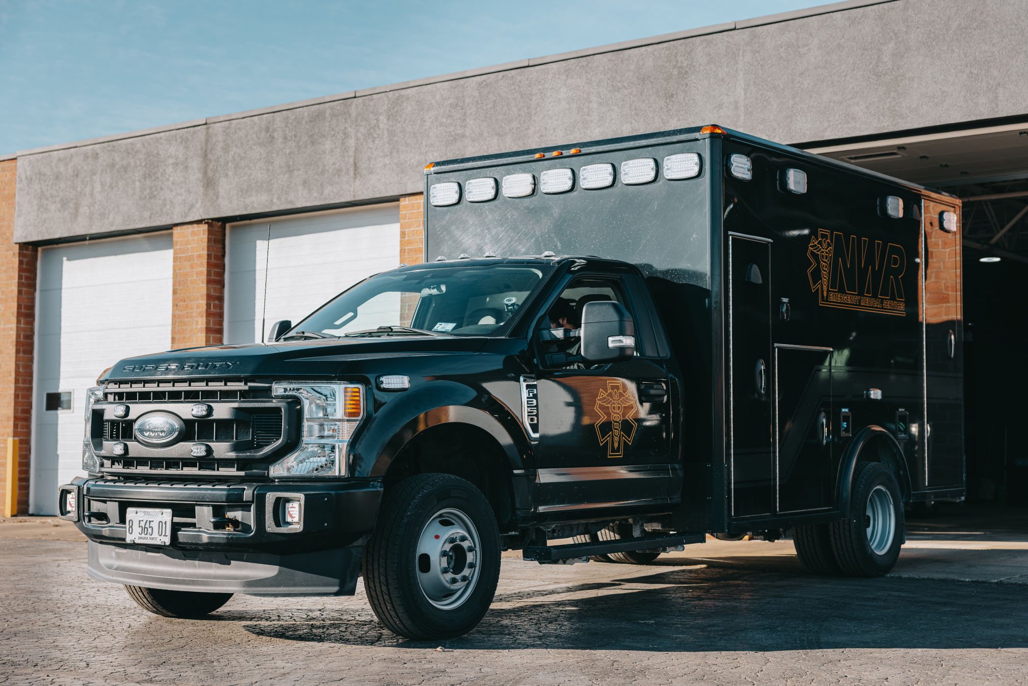 Black Ford F-350 emergency medical services truck parked outside a building with garage doors.