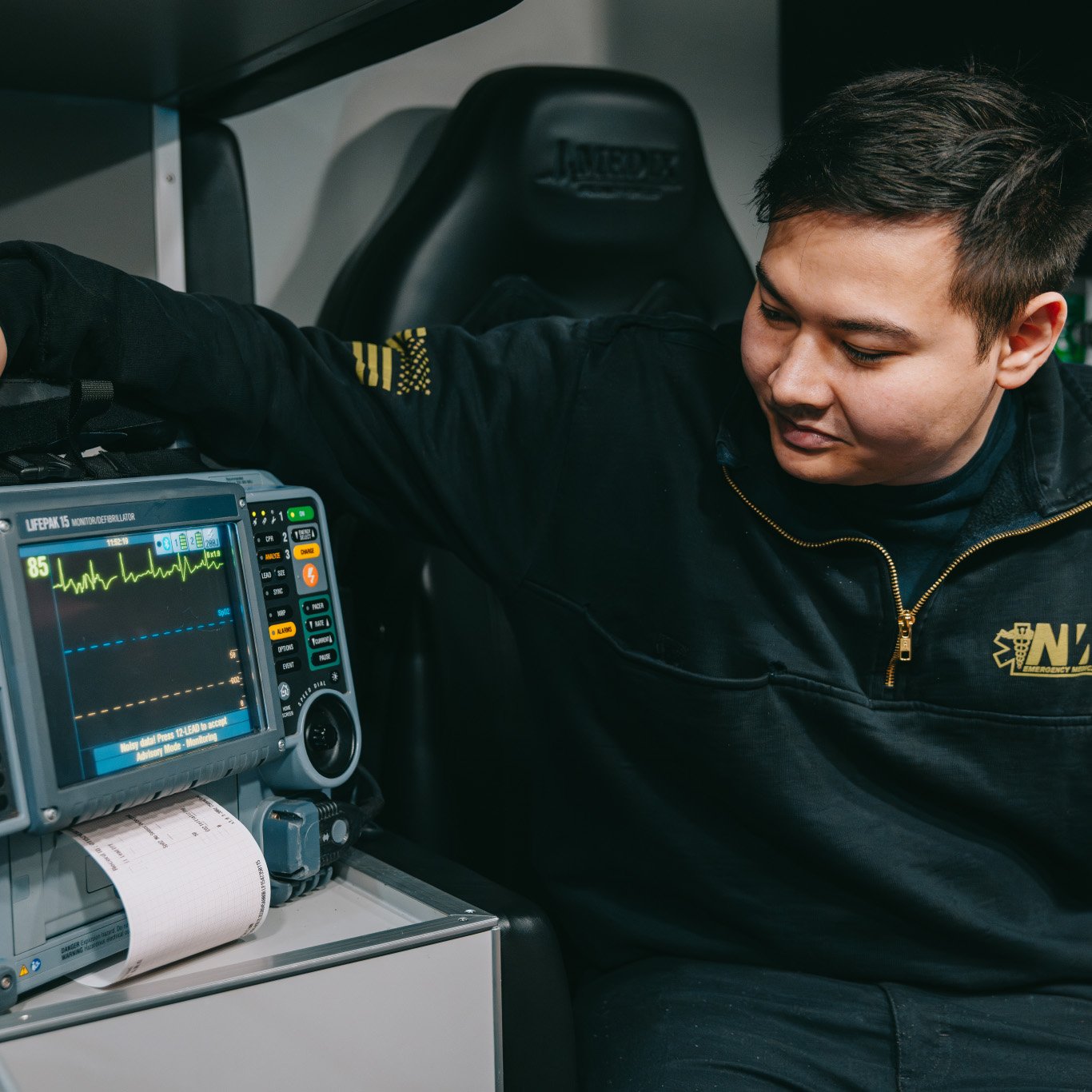 Emergency medical technician monitoring a LIFEPAK 15 defibrillator with heart rate displayed.