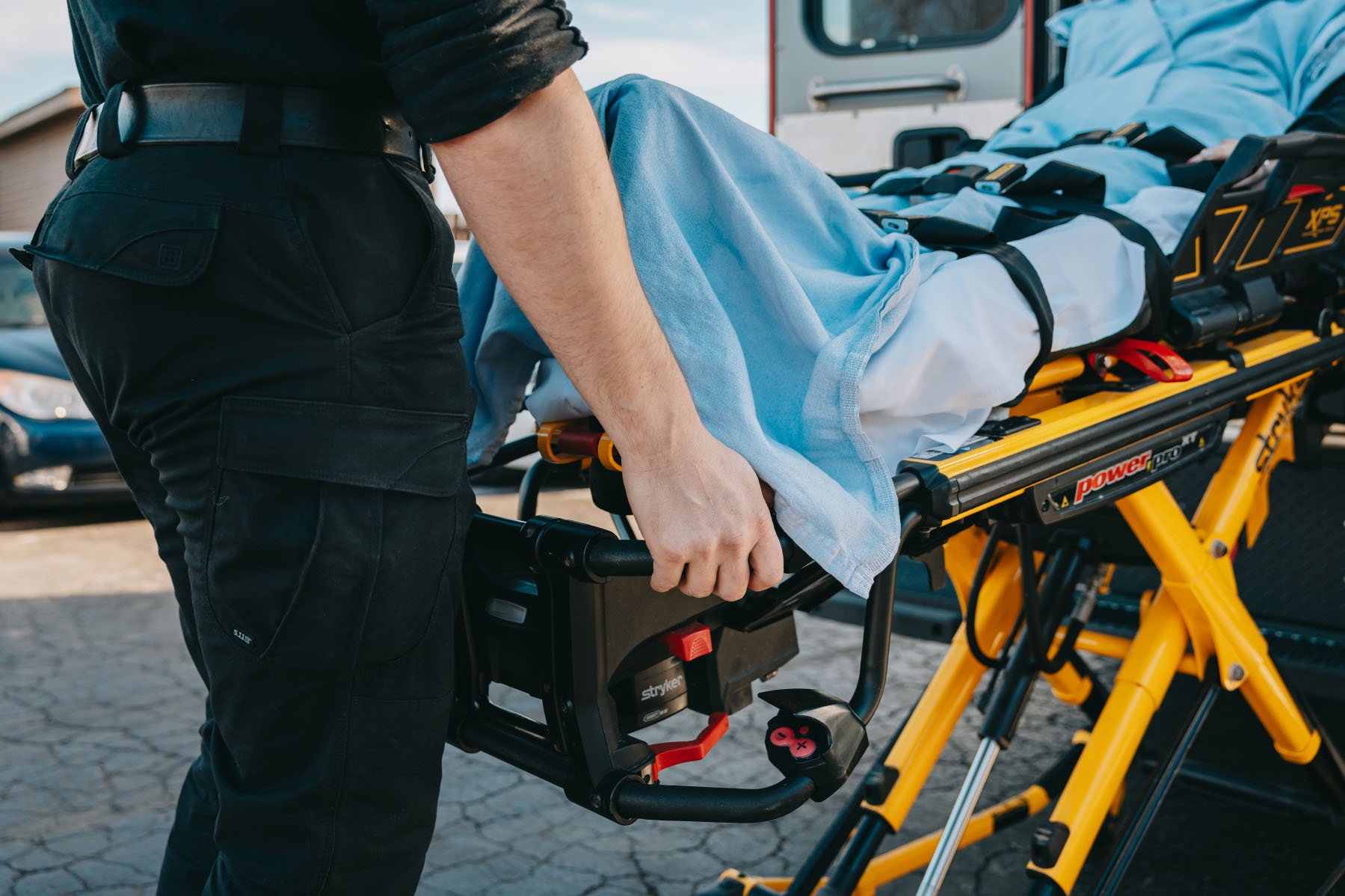Paramedic pushing a patient on a stretcher covered with a blue blanket toward an ambulance.