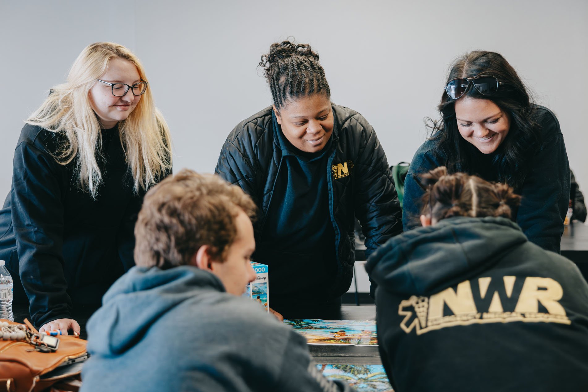 Five people gathered around a table working on a jigsaw puzzle, smiling and engaged.