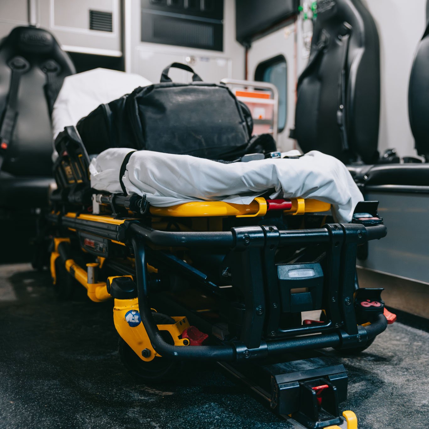 Stretcher with a black bag and white sheet inside an ambulance.