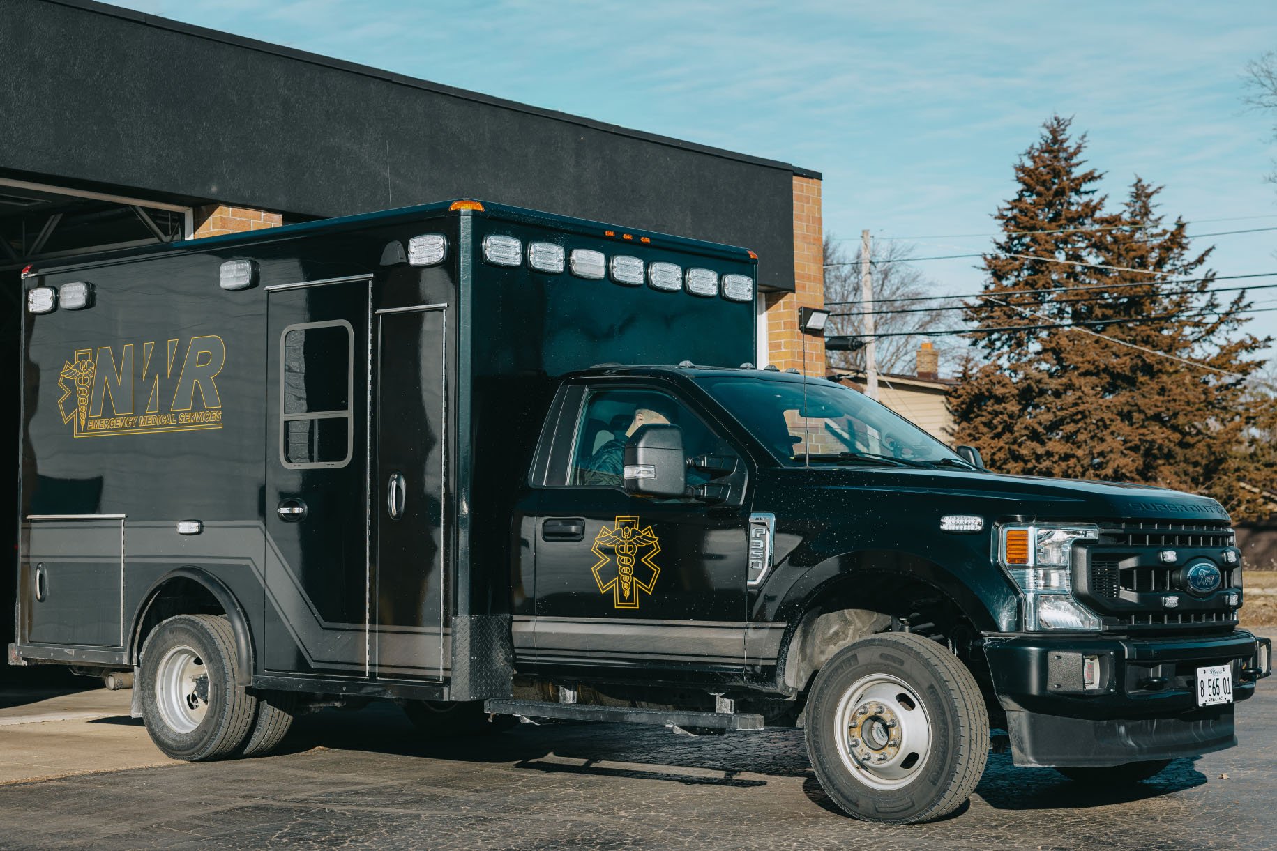 Black Ford emergency medical services vehicle with NWR branding parked outside a building.