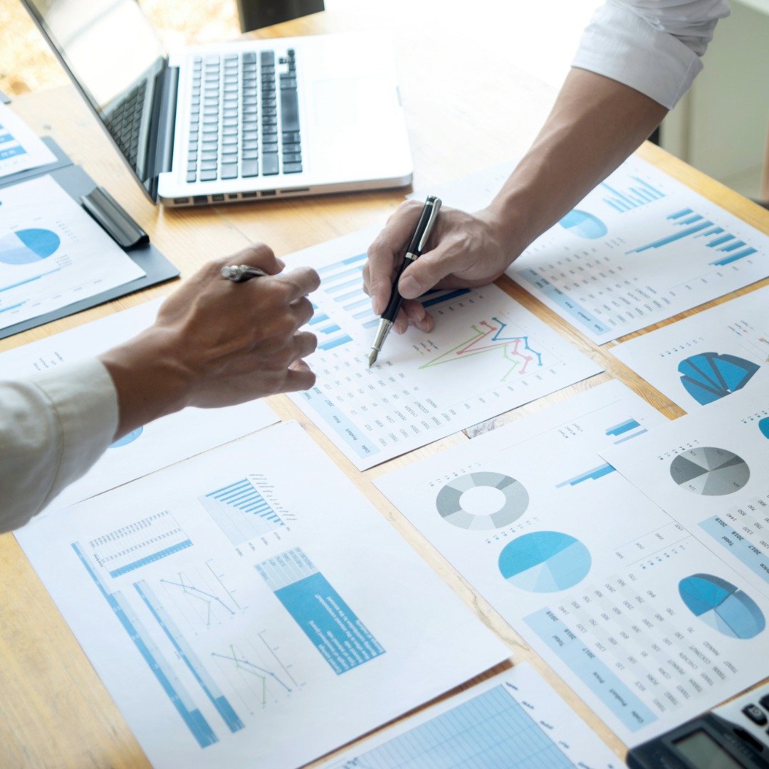 Two people analyzing financial charts and graphs on paper with a laptop nearby.