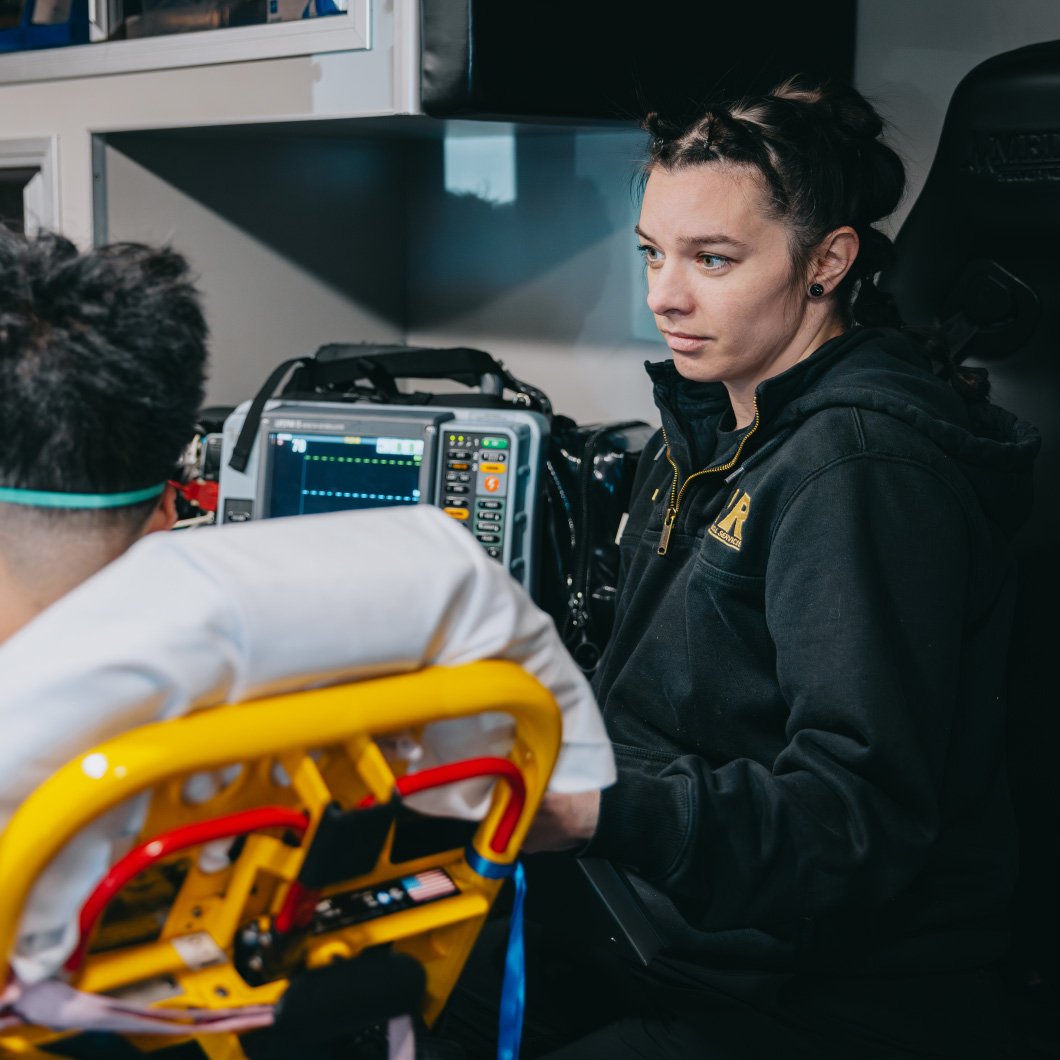 Emergency medical technician attentively monitoring patient vital signs on equipment inside an ambulance.