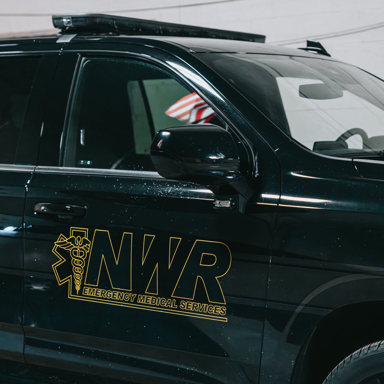 Black emergency medical services vehicle with NWR logo on the door and a medical caduceus symbol.