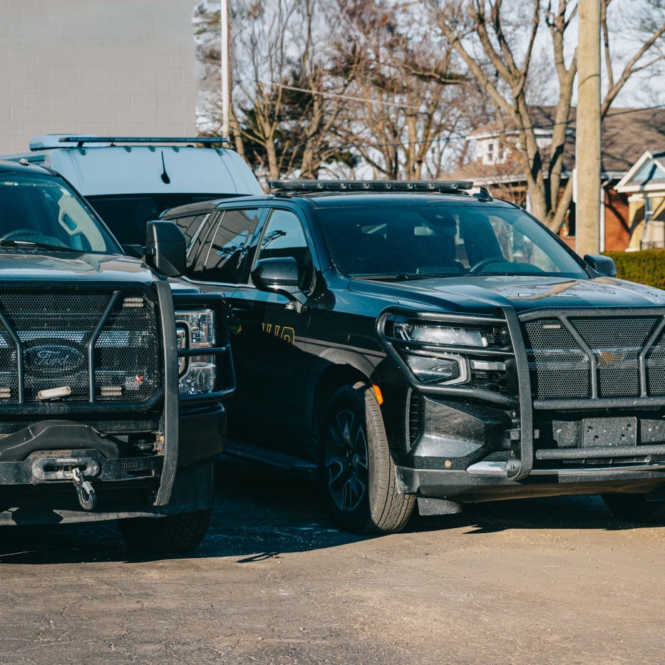 Two black police SUVs with push bumpers parked outdoors on a sunny day.