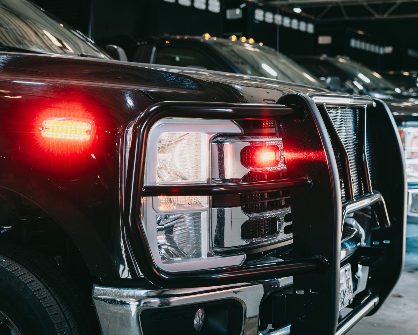 Close-up of the front left side of a black pickup truck showing illuminated red and amber lights and a metal grille guard.