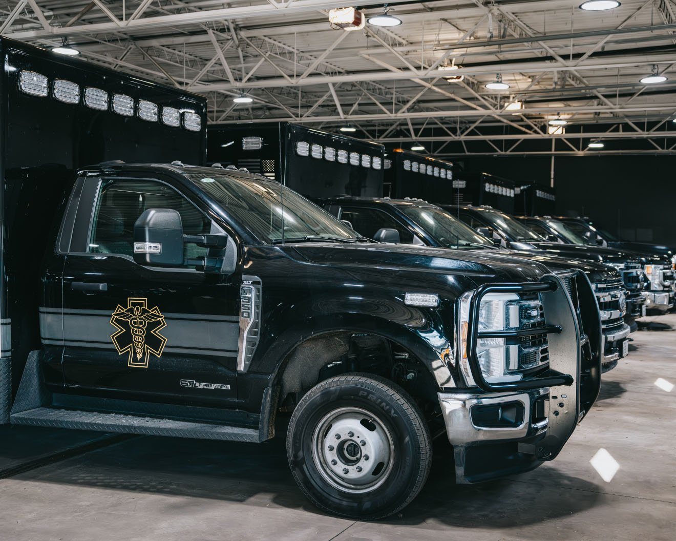 Row of black emergency response trucks with medical symbol parked inside a spacious, well-lit warehouse.